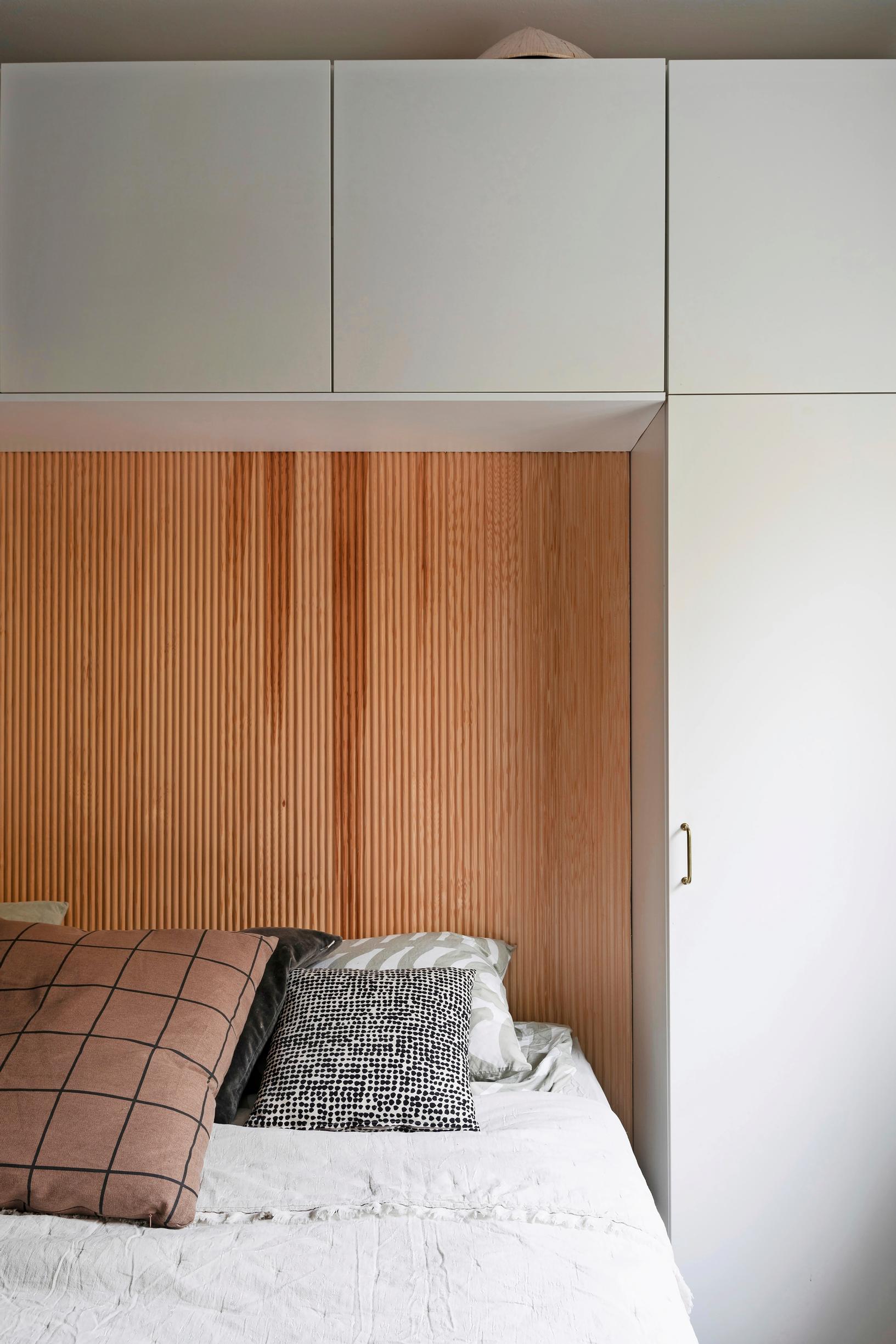 The wall at the head of the bed features finger-joint paneling, flanked by tall built-in cabinets on the sides and shorter ones above.