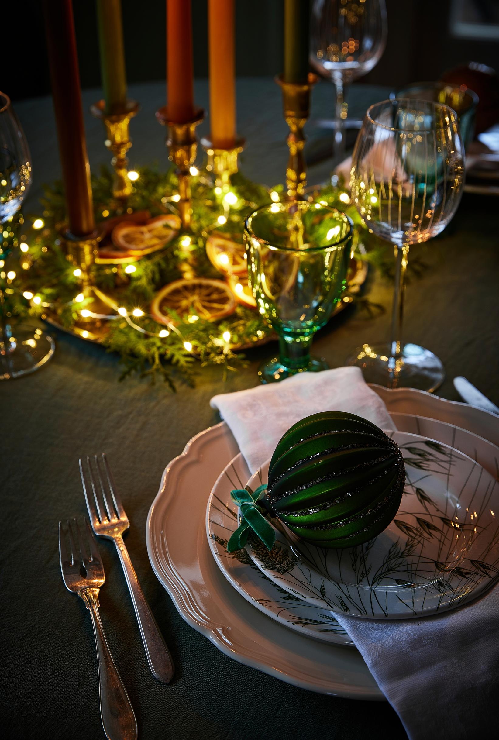 In the center of the round table, an arrangement of conifer branches, string lights, and toasted orange slices.
