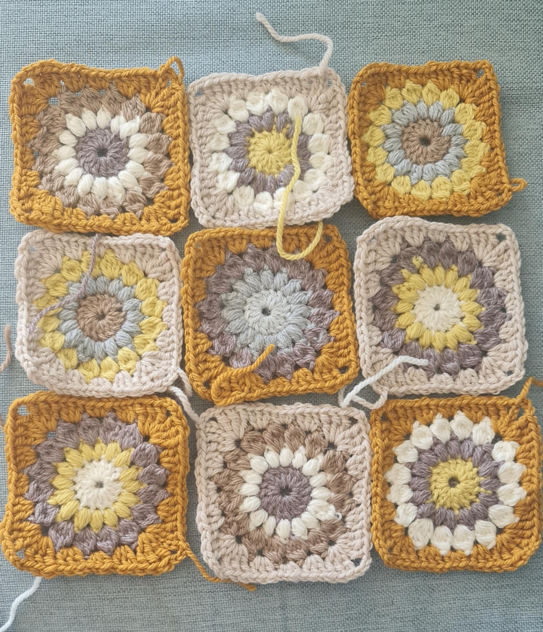 Yellow and orange-hued crocheted squares called sunflower squares, laid out on a table.