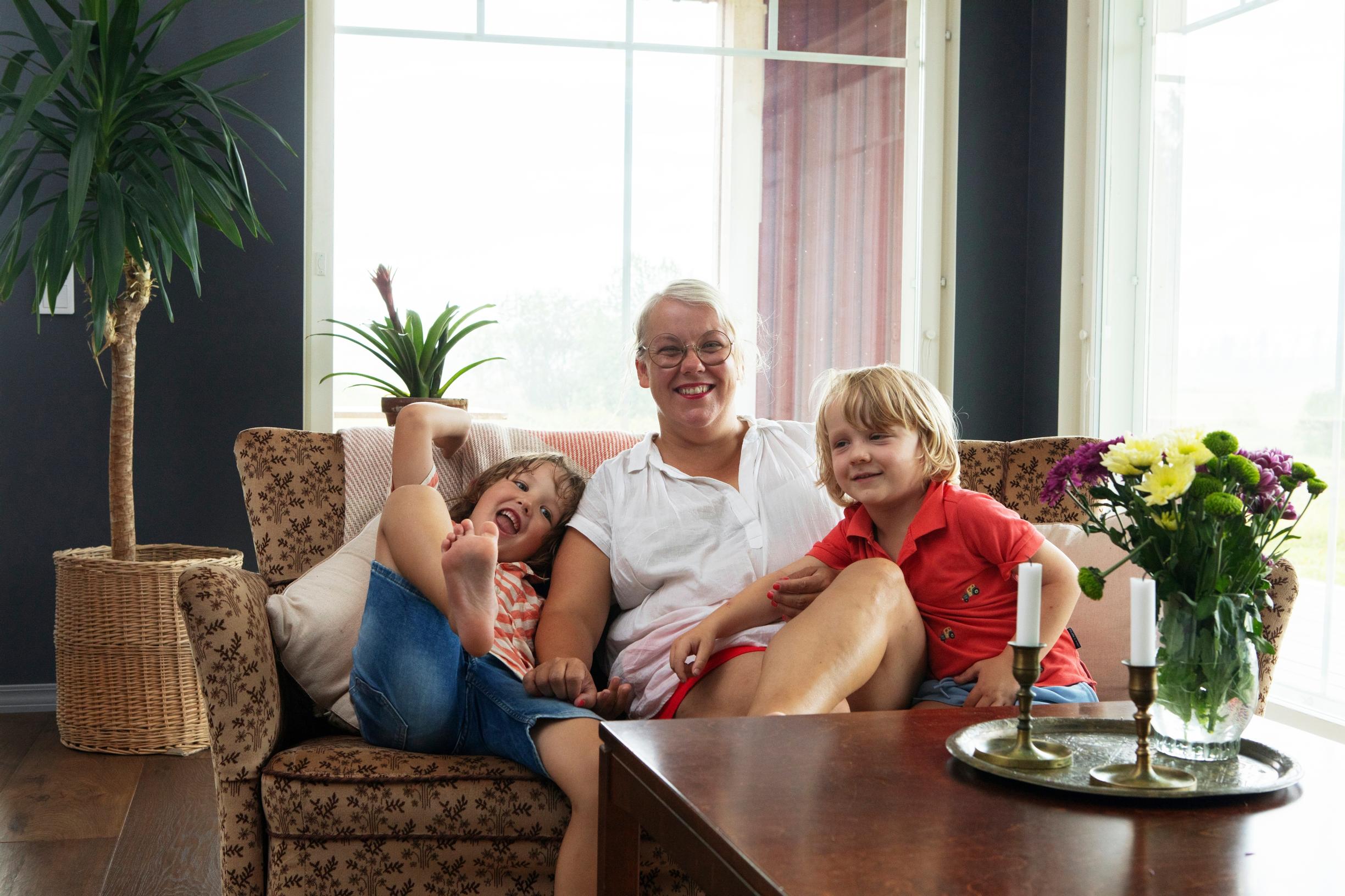 A woman and two children sitting on a sofa in front of a window.