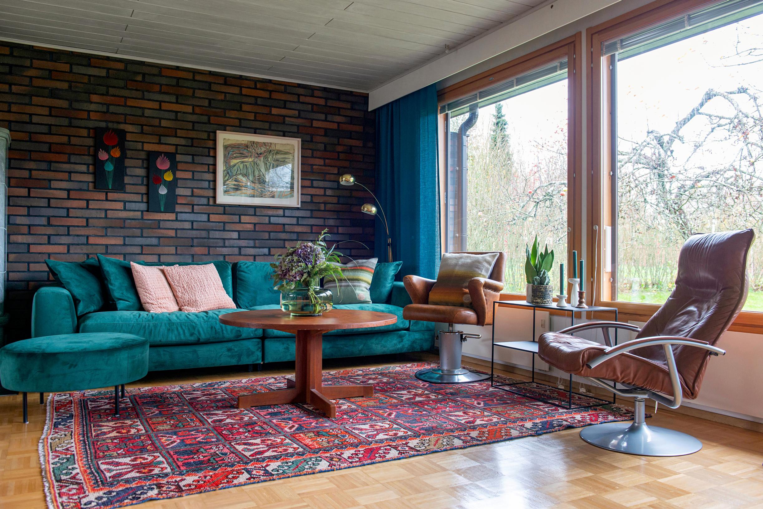 A turquoise sofa sits against the dark grayish-red brick wall of the living room, with a round coffee table in front.