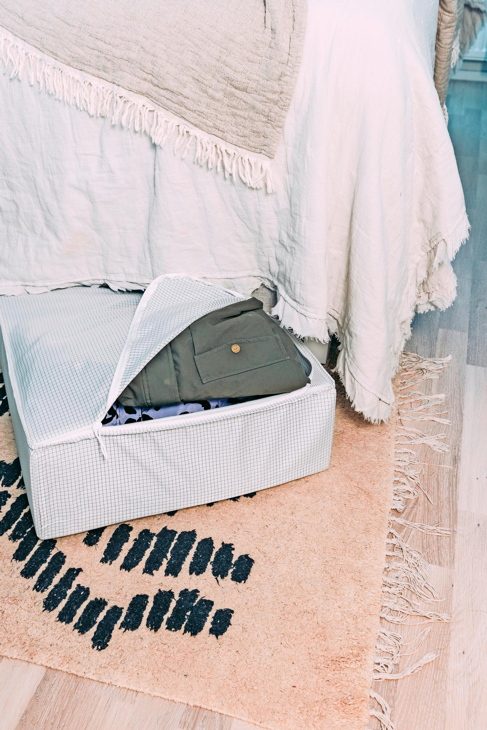 An under-bed box with a zip-top peeks out from beneath the bed, showing clothes inside.