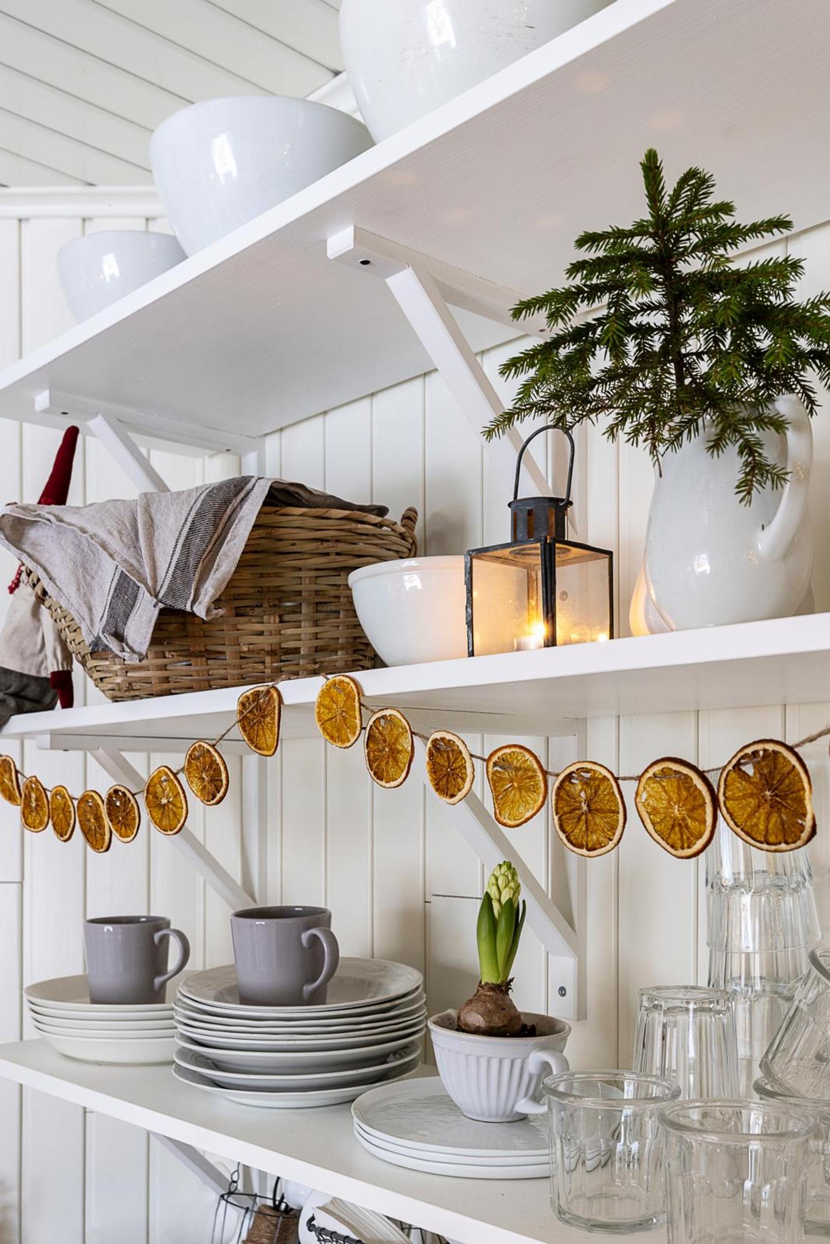 Dried orange slices are strung on jute twine and hung to decorate a dish shelf.