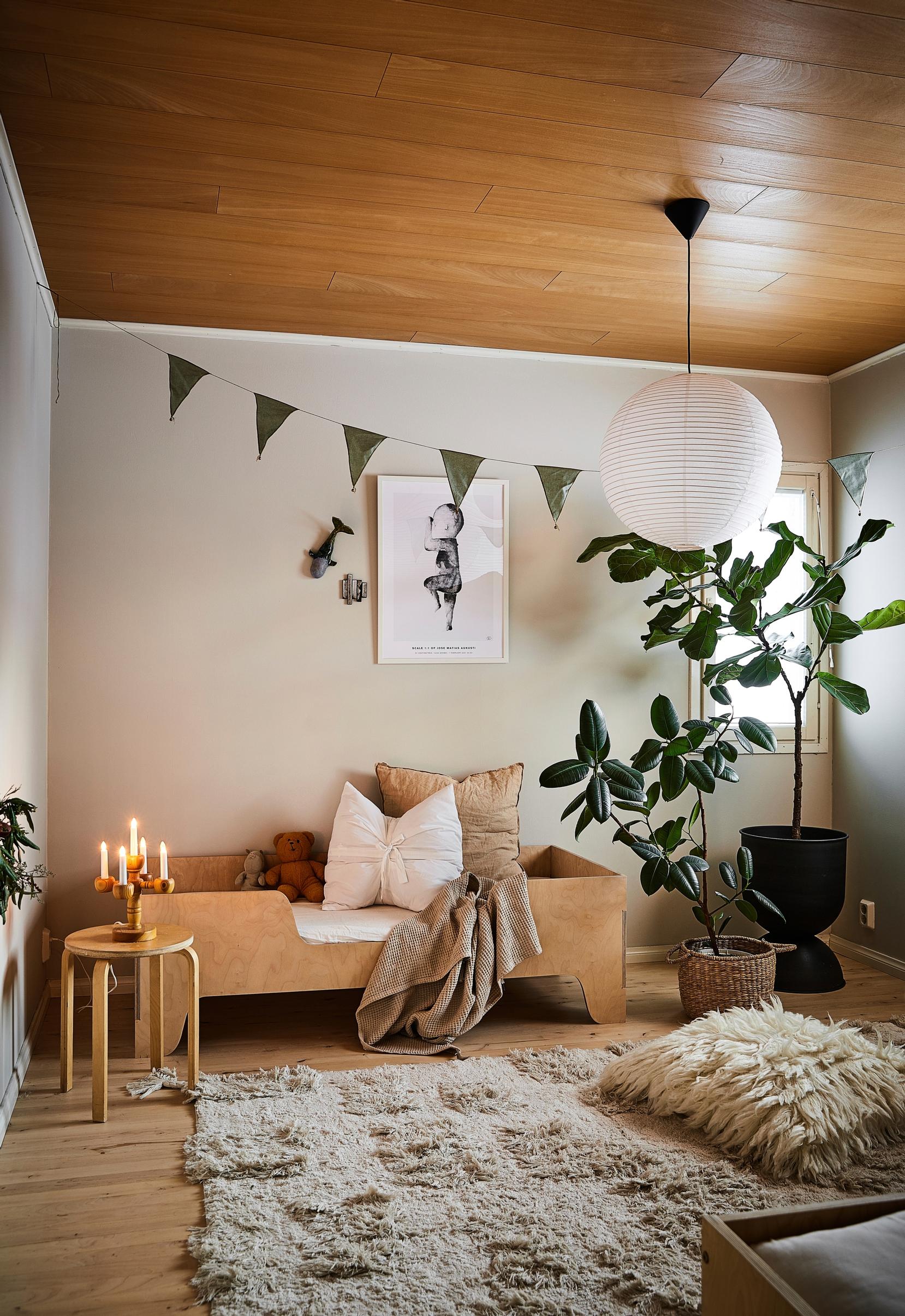 A houseplant, child’s bed, rug, cushion, pennant banner, rice paper lamp, stool, and a candle holder