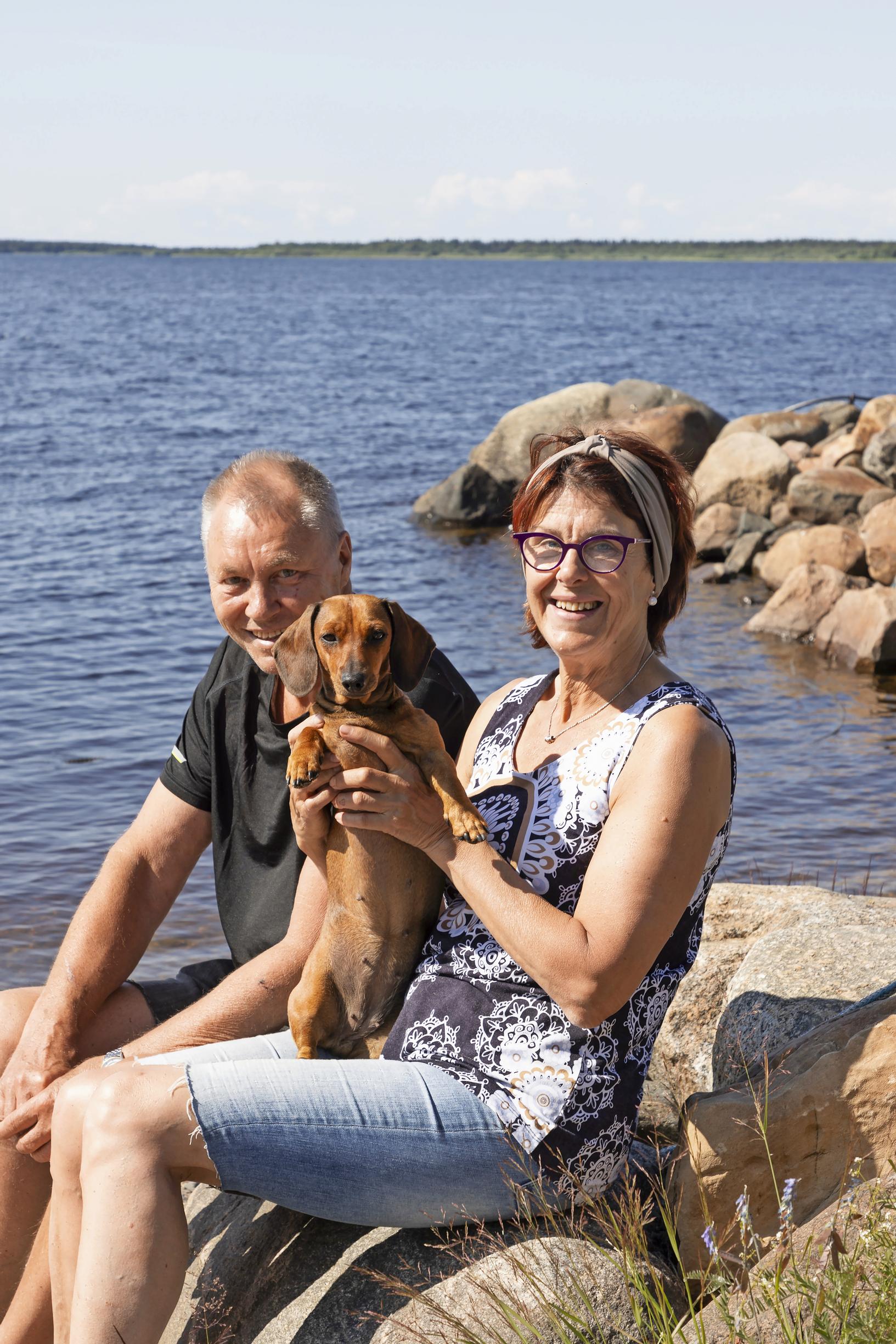 Marita Kumpulainen and Eki Nikkanen by their island cottage’s shore on Selkäsaari, with a dachshund in their arms