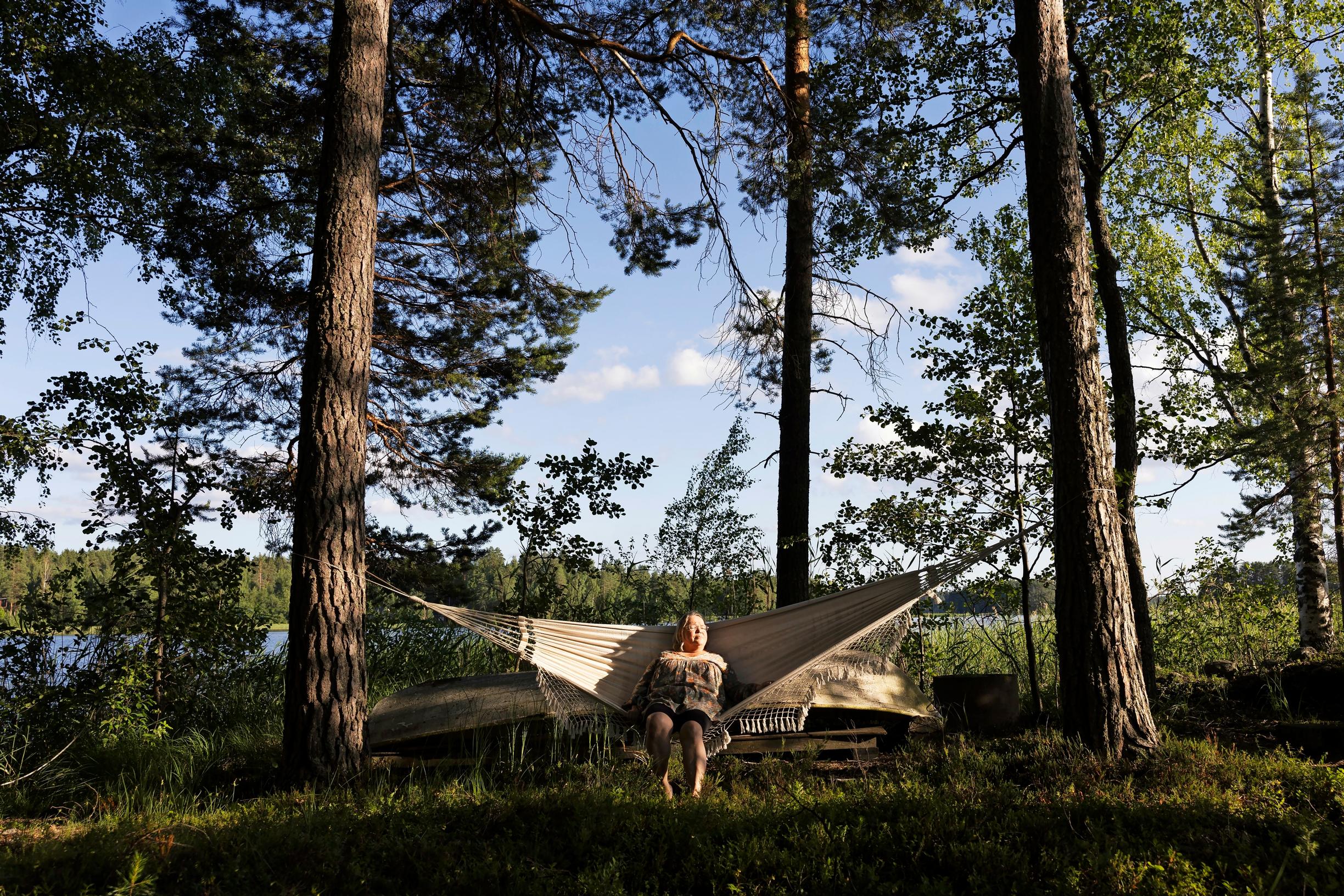 Helena sits in a large hammock, tall trees