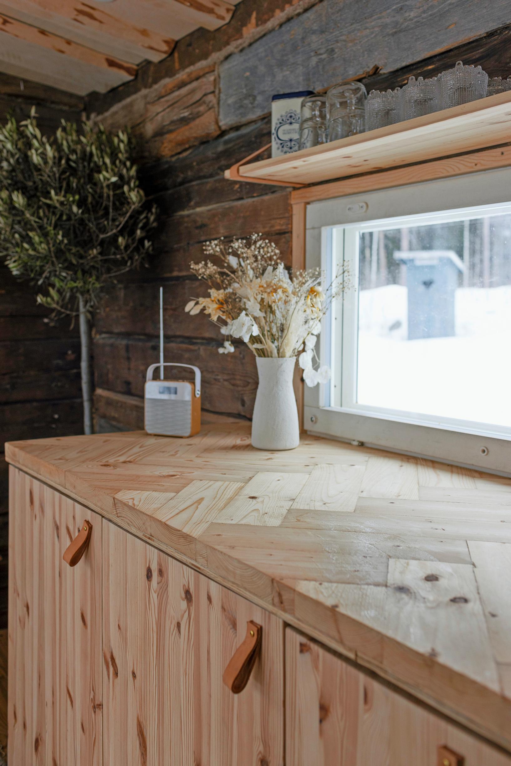 A pine cabinet under a window, an outhouse visible outside, and a snowy landscape.