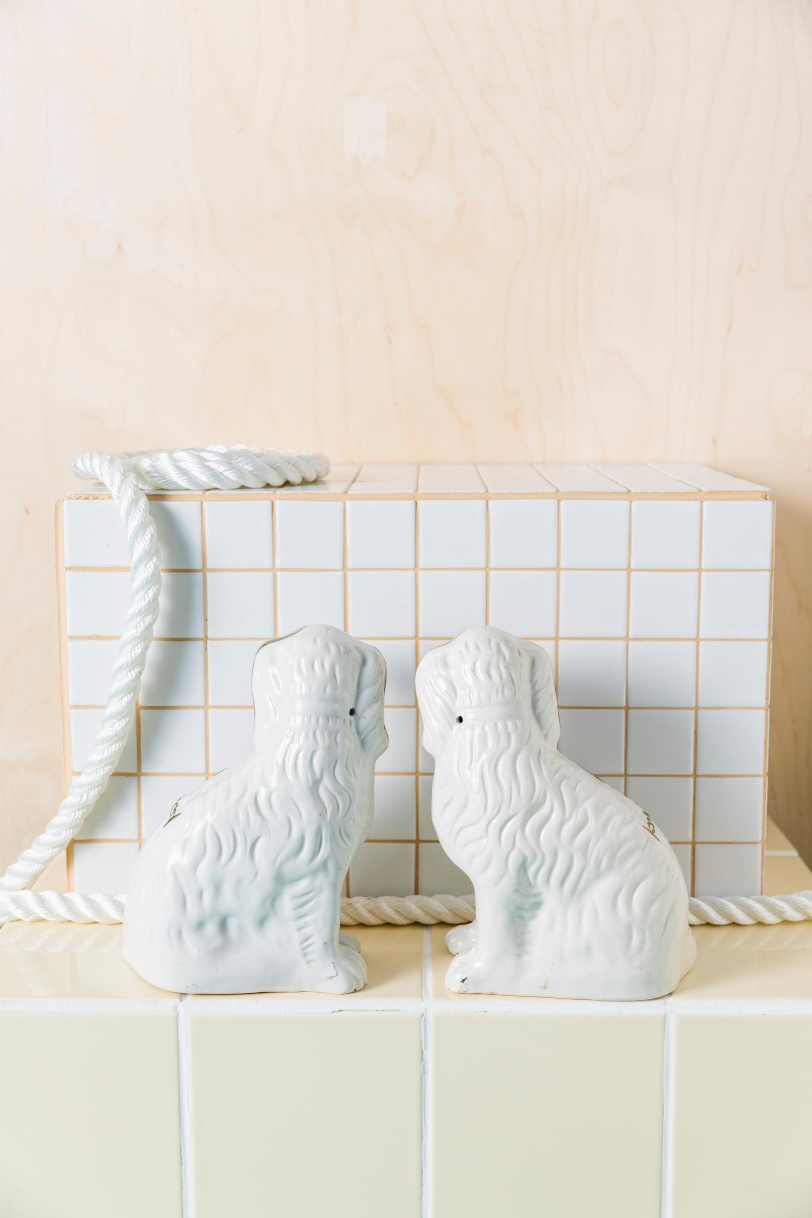 white Staffordshire dog figurines seen from behind on a tiled shelf 