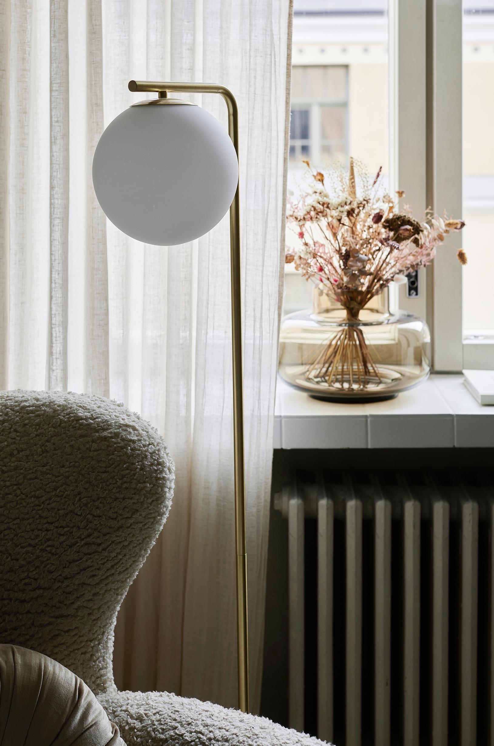 A floor lamp with a round shade in front of the window