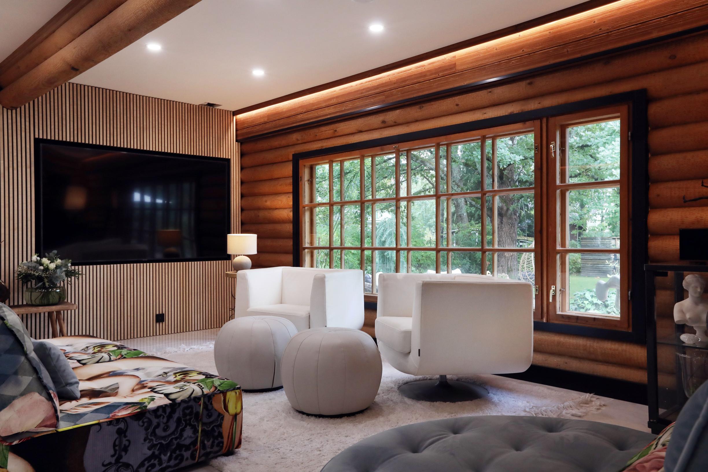 The living room has large pane windows, white armchairs, and a wall-mounted TV.