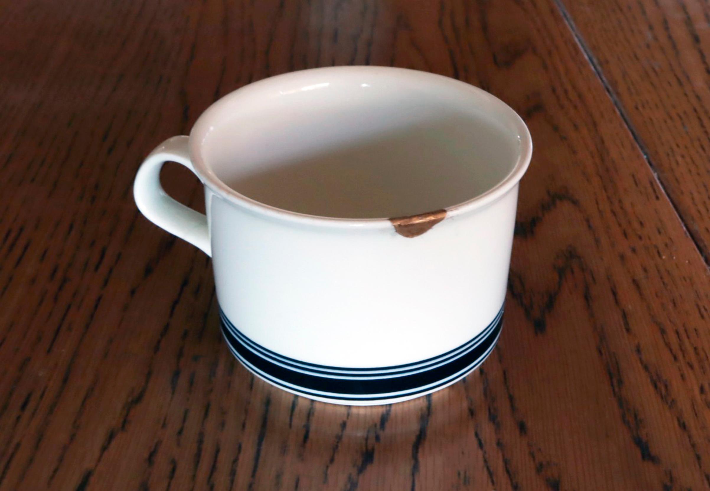 A coffee cup repaired with the kintsugi technique on a table.