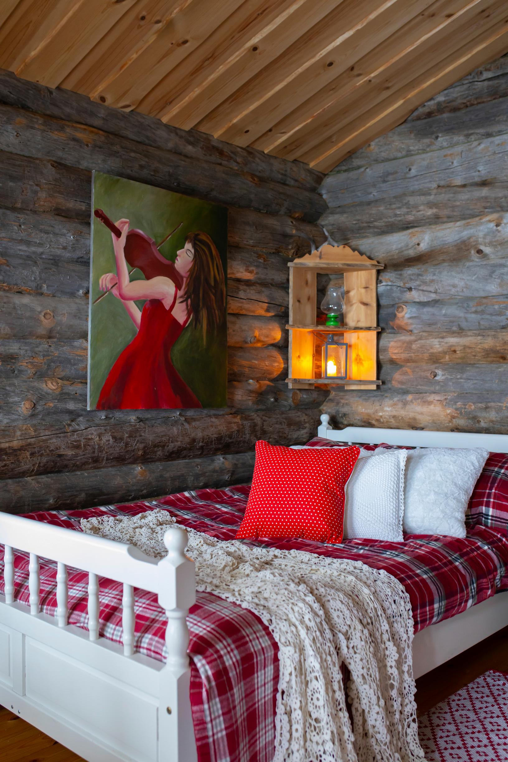 A double bed in the kelo cabin with red and white linens, with a painting on the wall.