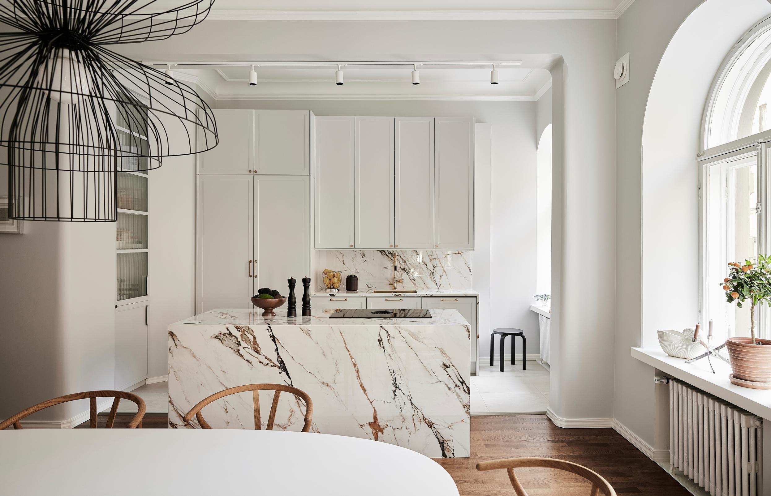 An open kitchen featuring a marble-patterned island and arched windows