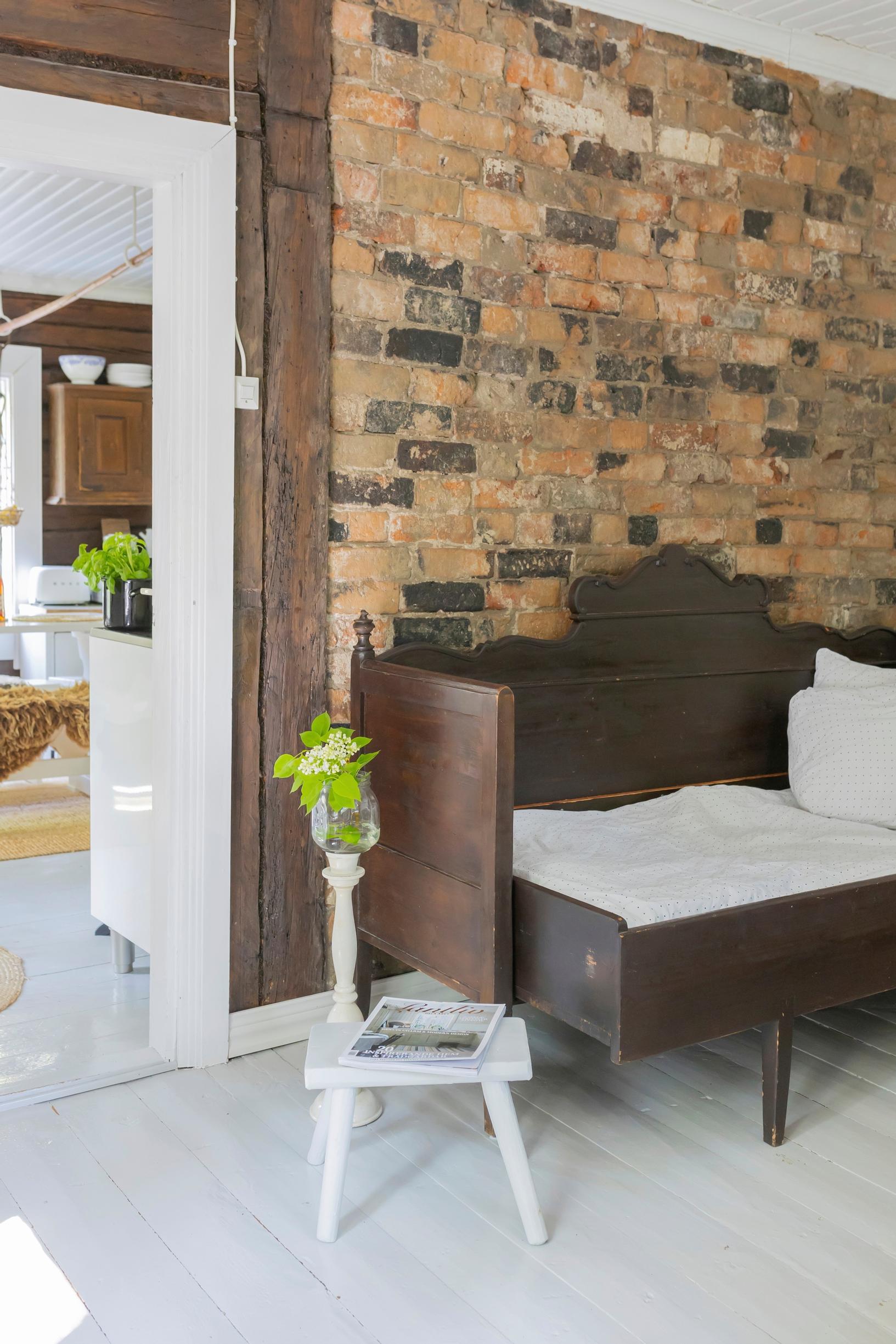 A wooden daybed stands before a mottled yellow, black, and gray brick wall.