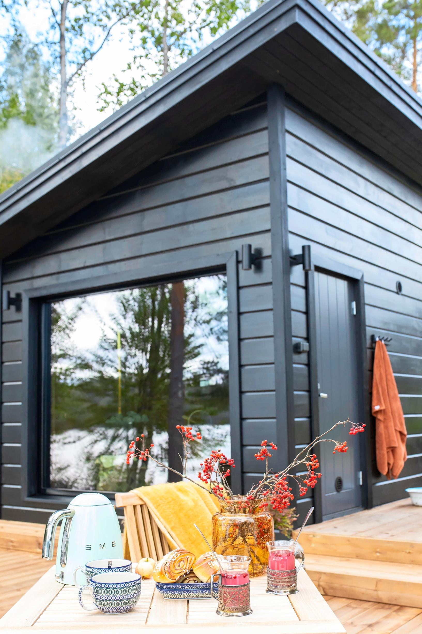 A black-painted sauna cottage with a terrace table in front