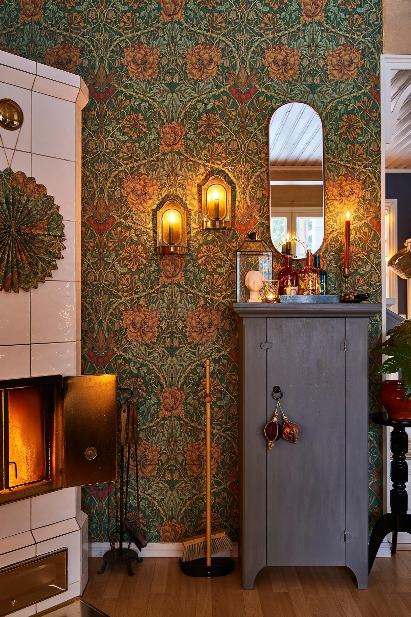 In the living room, the walls feature green William Morris wallpaper, a tile stove, and an old cabinet.