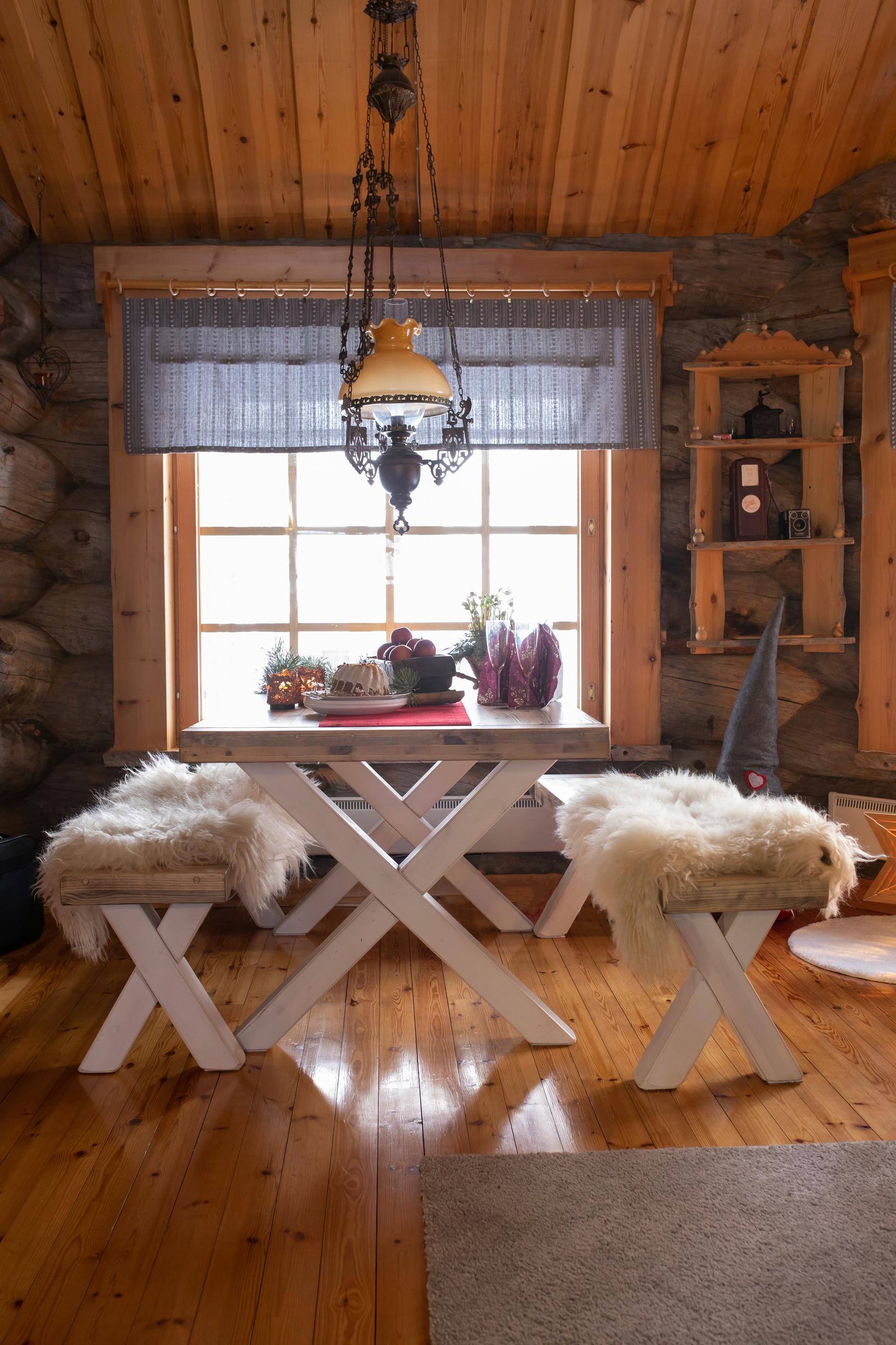 Fur throws on bench seats, a table and window, an oil lamp, and a wall cabinet.