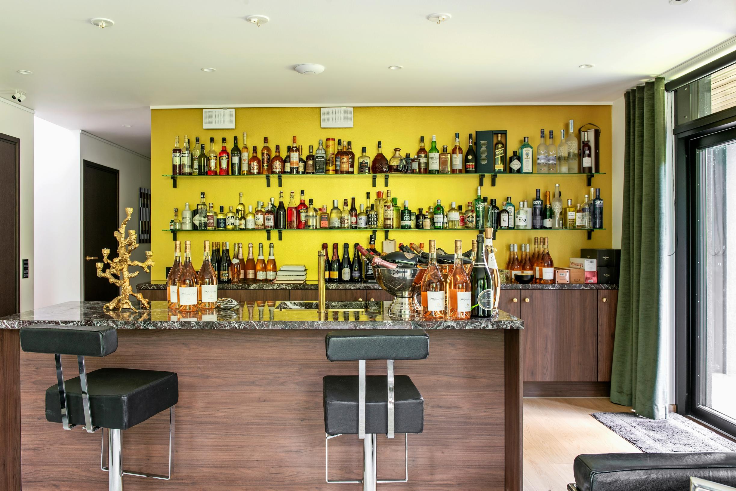 In the downstairs bar-lounge, a yellow wall with rows of bottles stored on open shelves