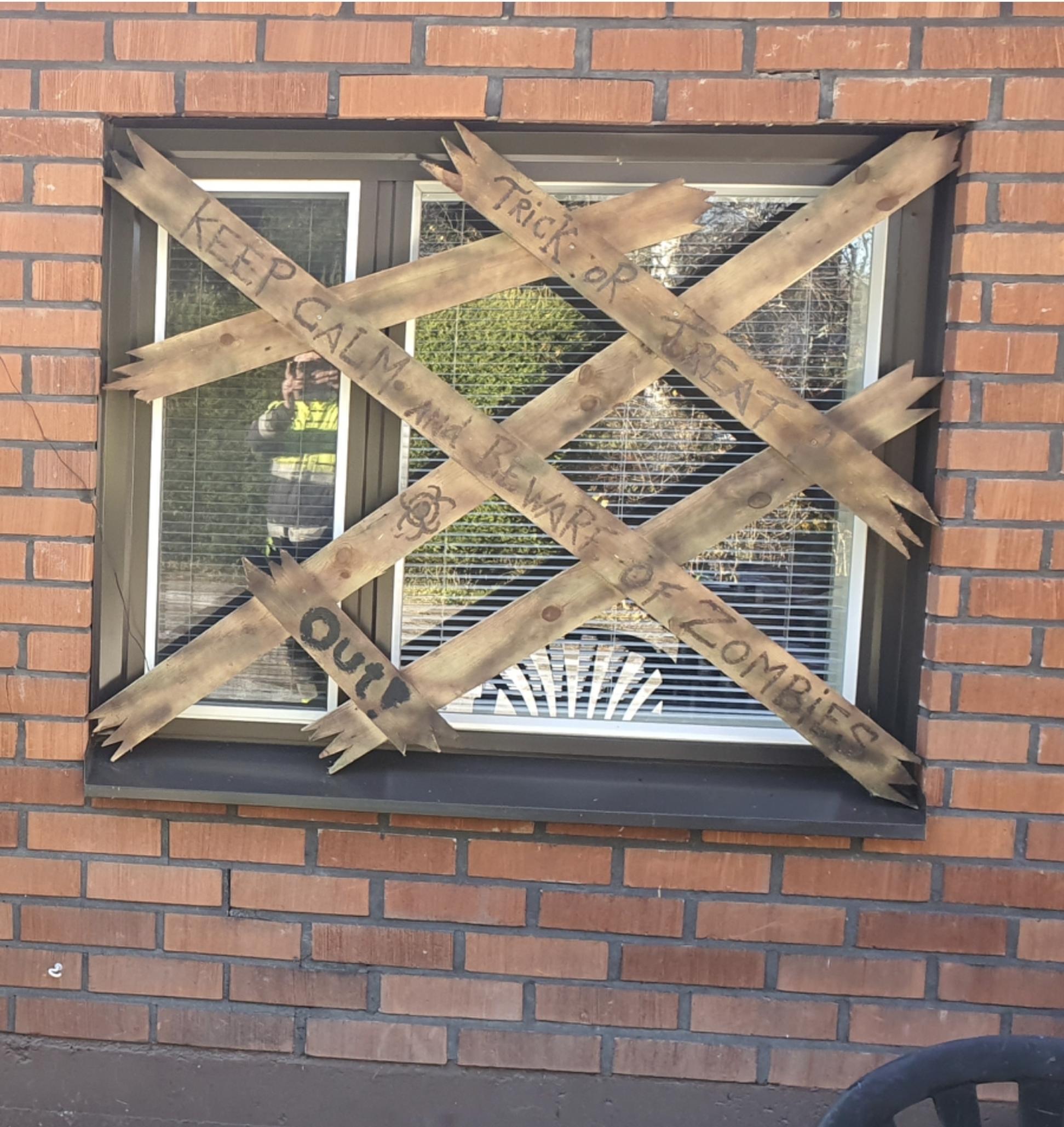 Boards placed in front of the window with text referencing zombies, stay away, keep out!