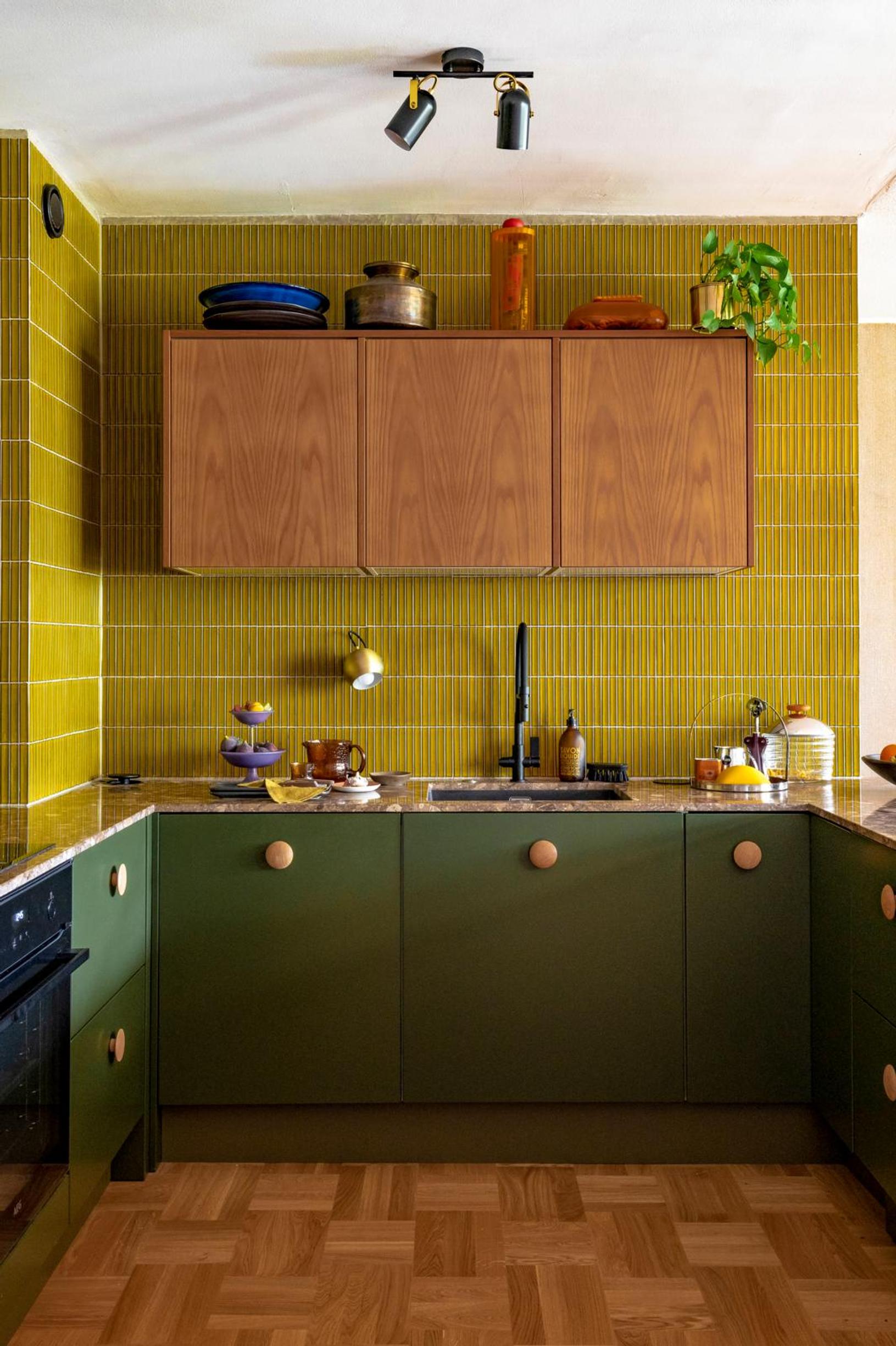 The olive green tiled wall features three upper cabinets. The pine green lower cabinets are in the shape of a U.