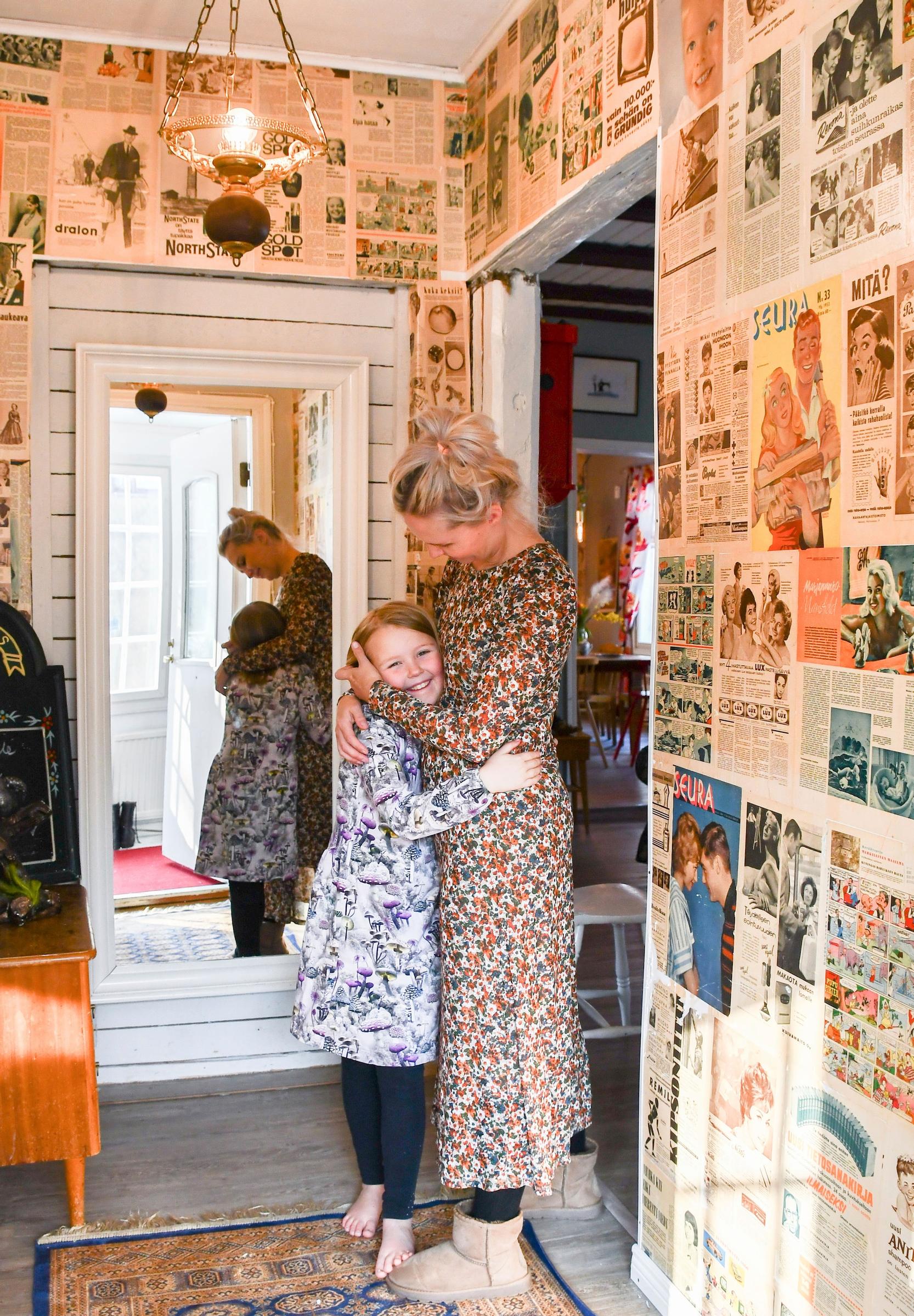 Suvi Kervinen hugging her child in the entryway. The walls are wallpapered with old newspapers.