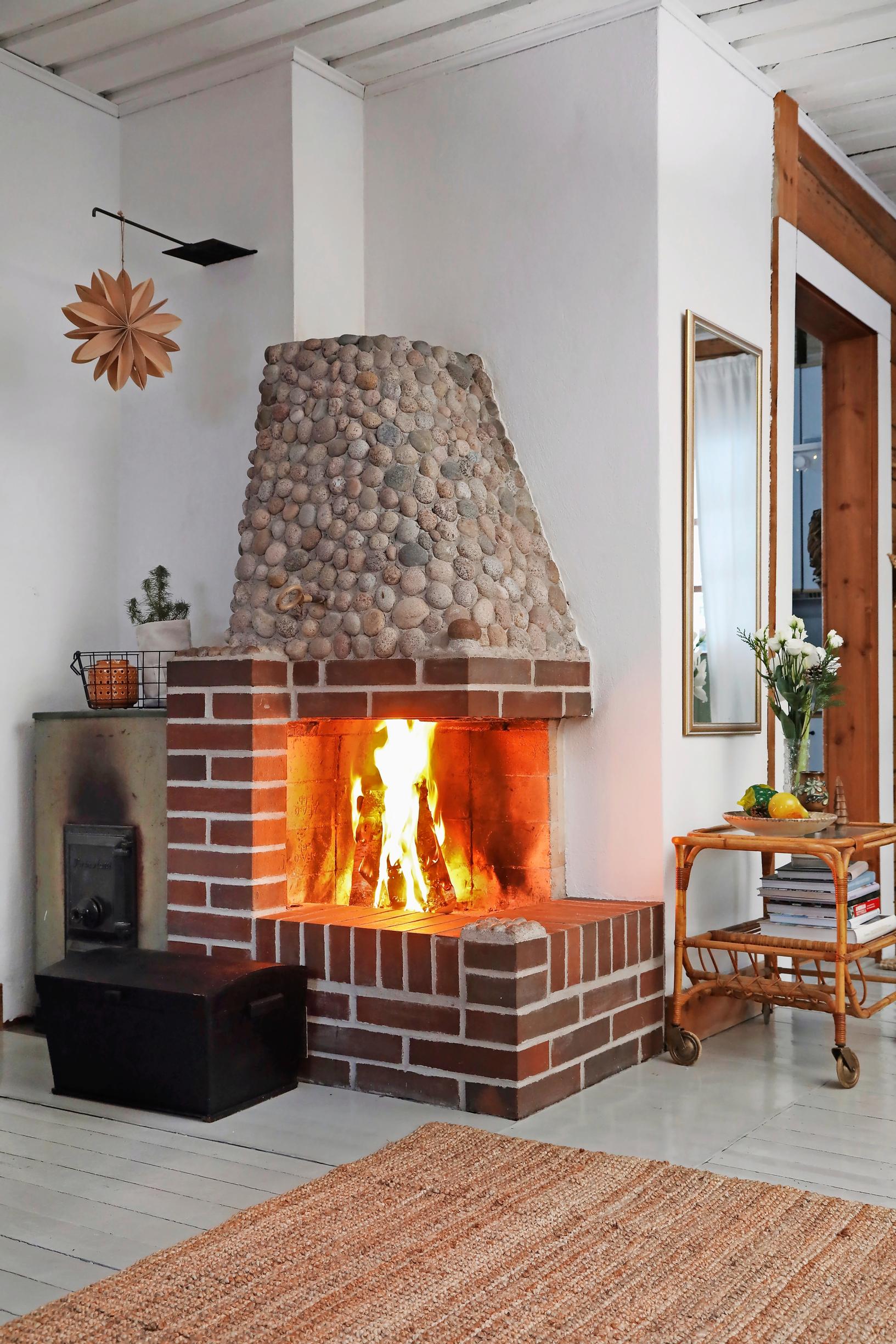 In Ulla Parviainen’s log cabin, a fire crackles in the open fireplace. Nearby are a wicker serving cart and a trunk.