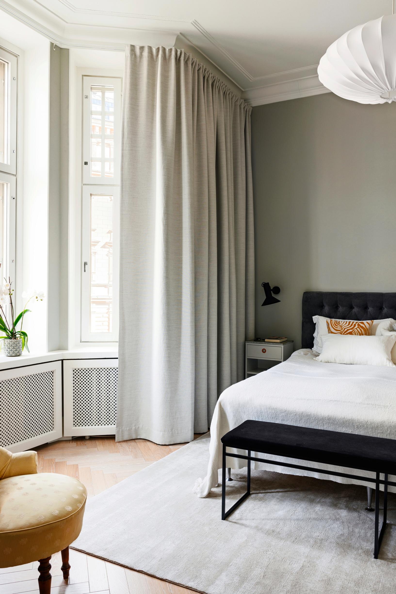 The bedroom’s bay windows with multiple panes, a double bed, and beige-painted walls.