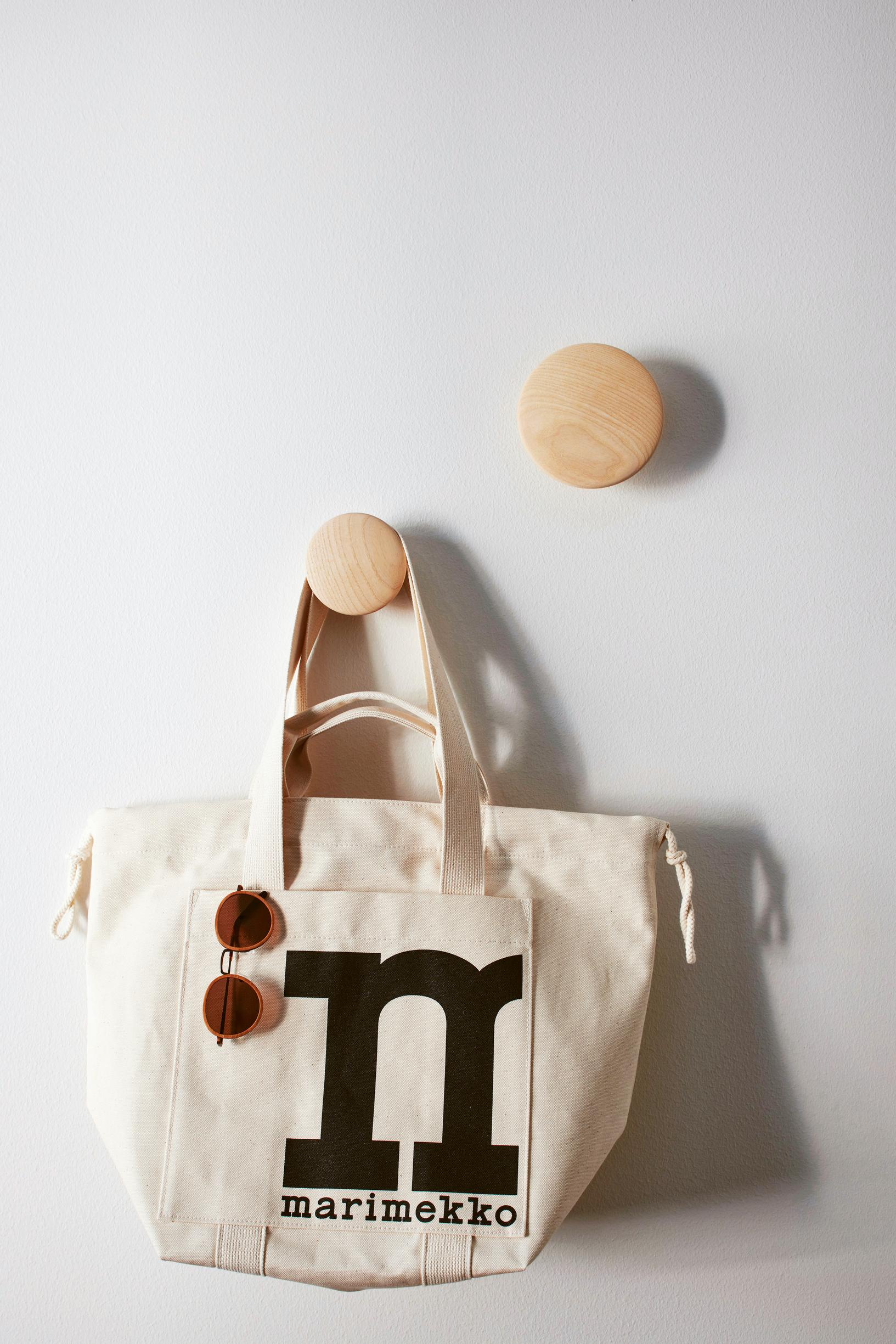 Round wooden wall hooks. One holds a Marimekko bag.
