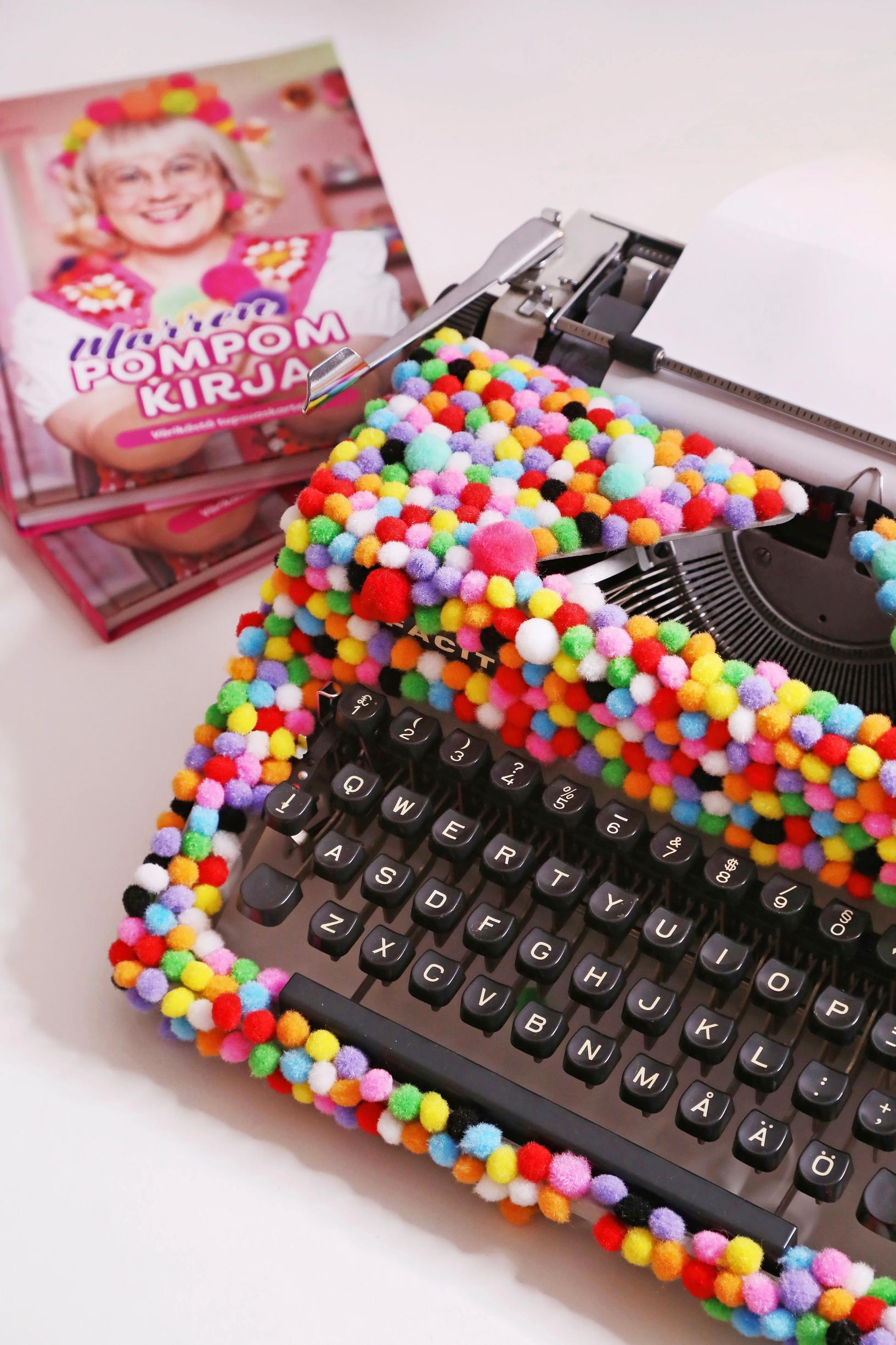 A typewriter decorated with pom-poms and Mari’s book.