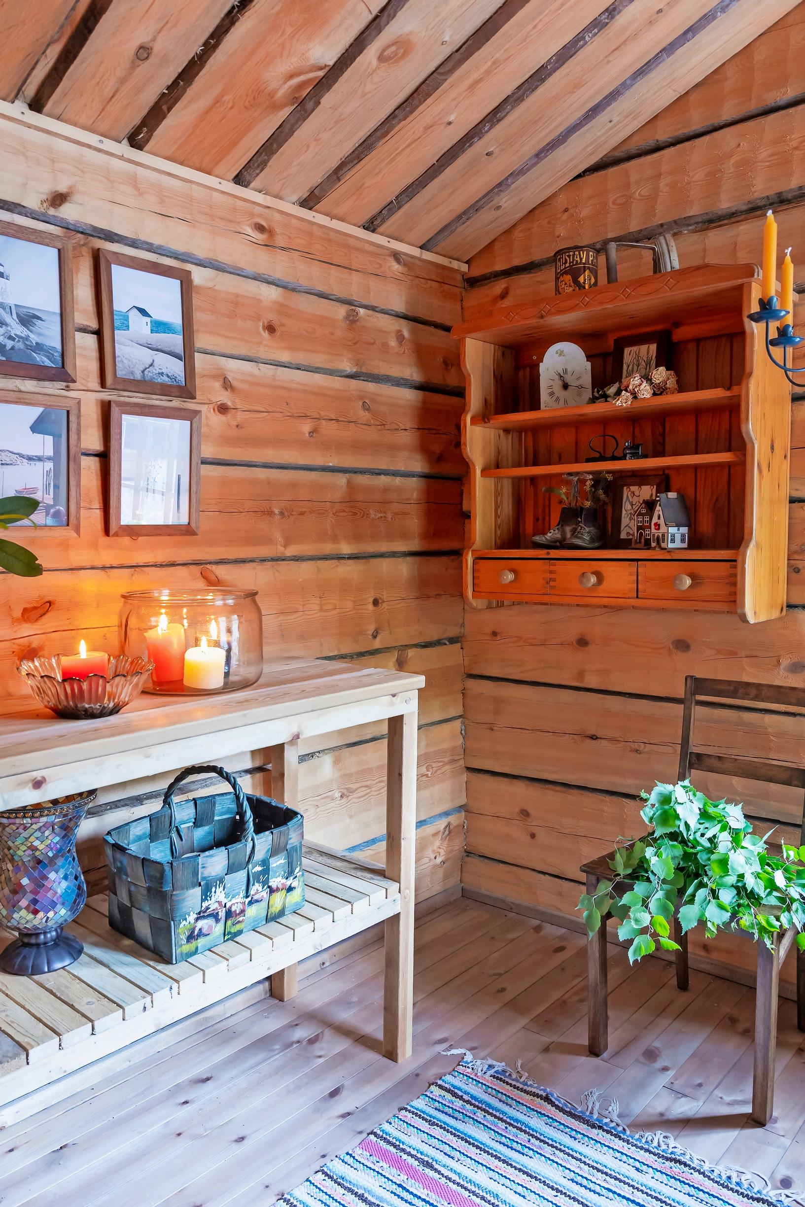 a wooden shelf on the wall, pictures, a log wall, and candles on a side table