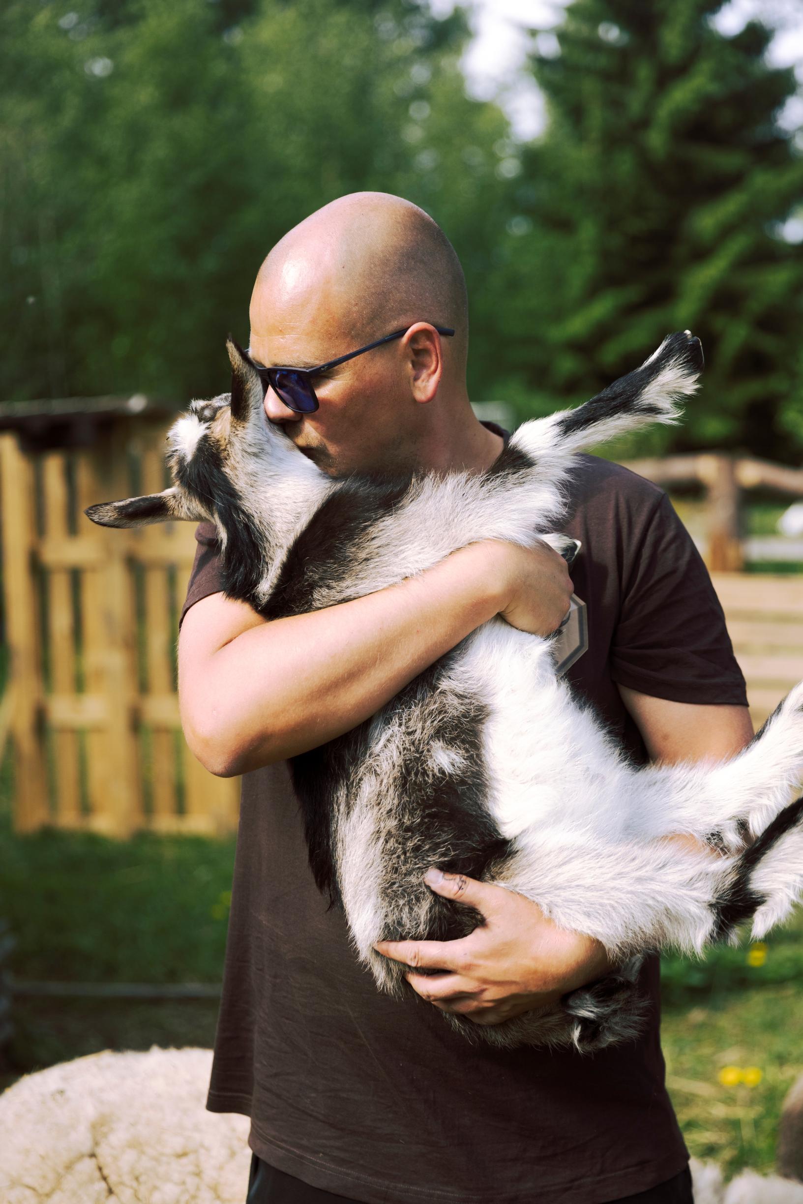 man holding a goat in his arms and kissing it