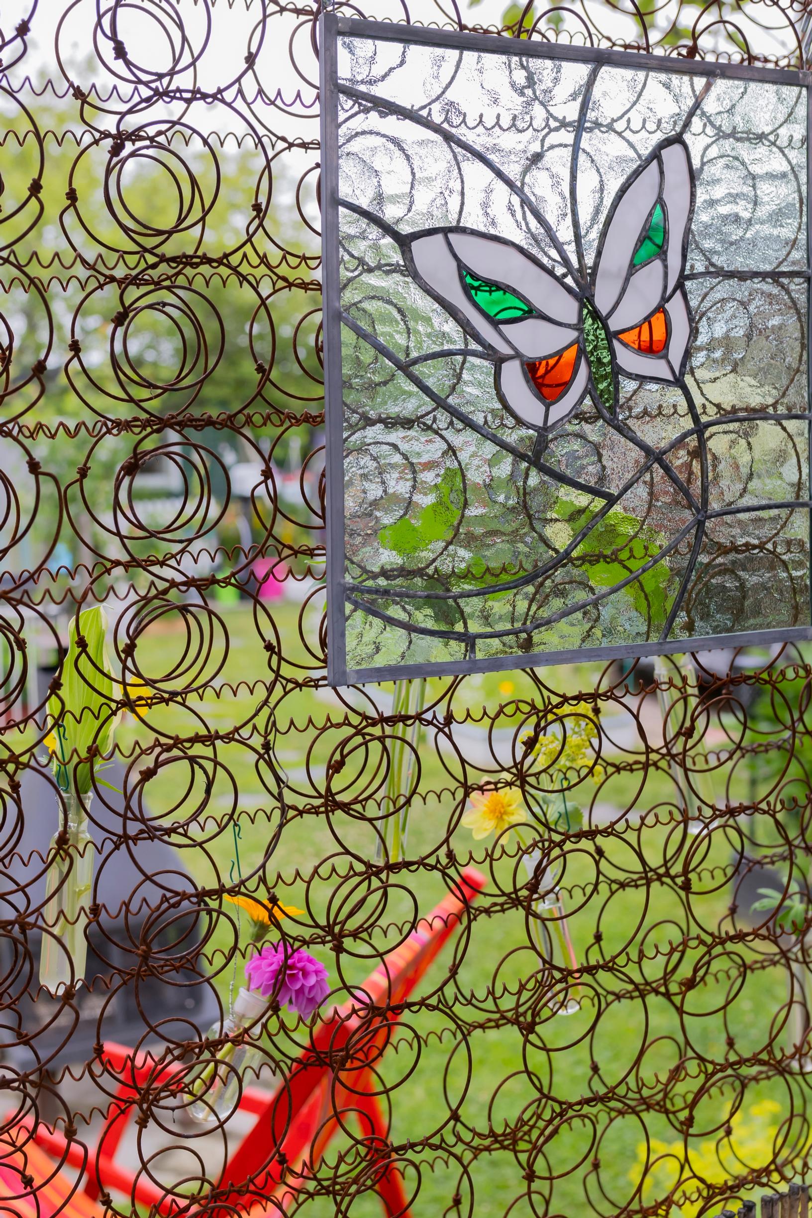 a butterfly-shaped pattern in a glass painting and a bed spring in an upright position serving as a trellis