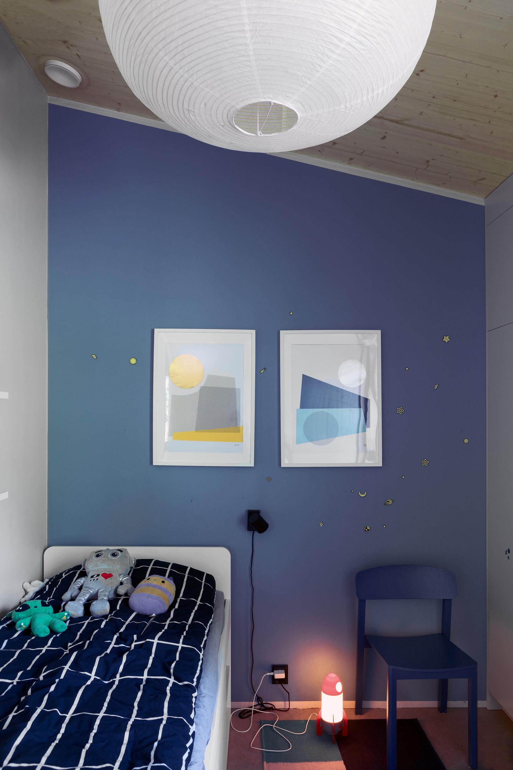 A bedroom with a bed and a wooden chair. The wall is painted blue.