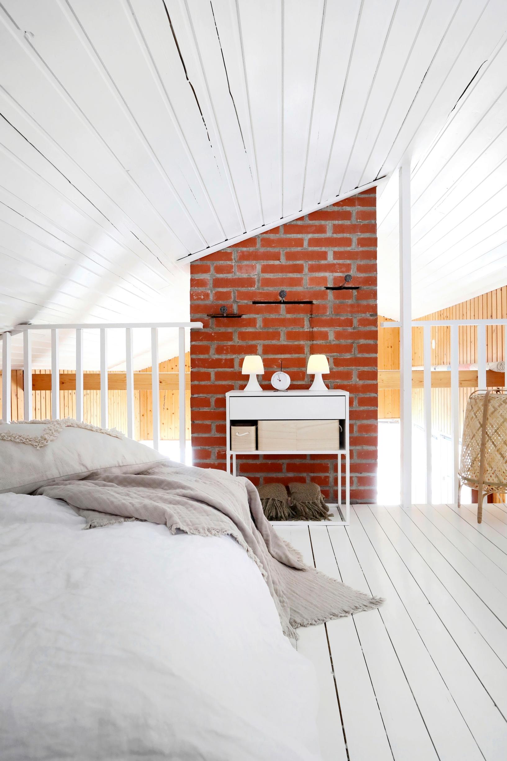 A low bed sits to the left under a sloping ceiling, with the chimney in the center background.