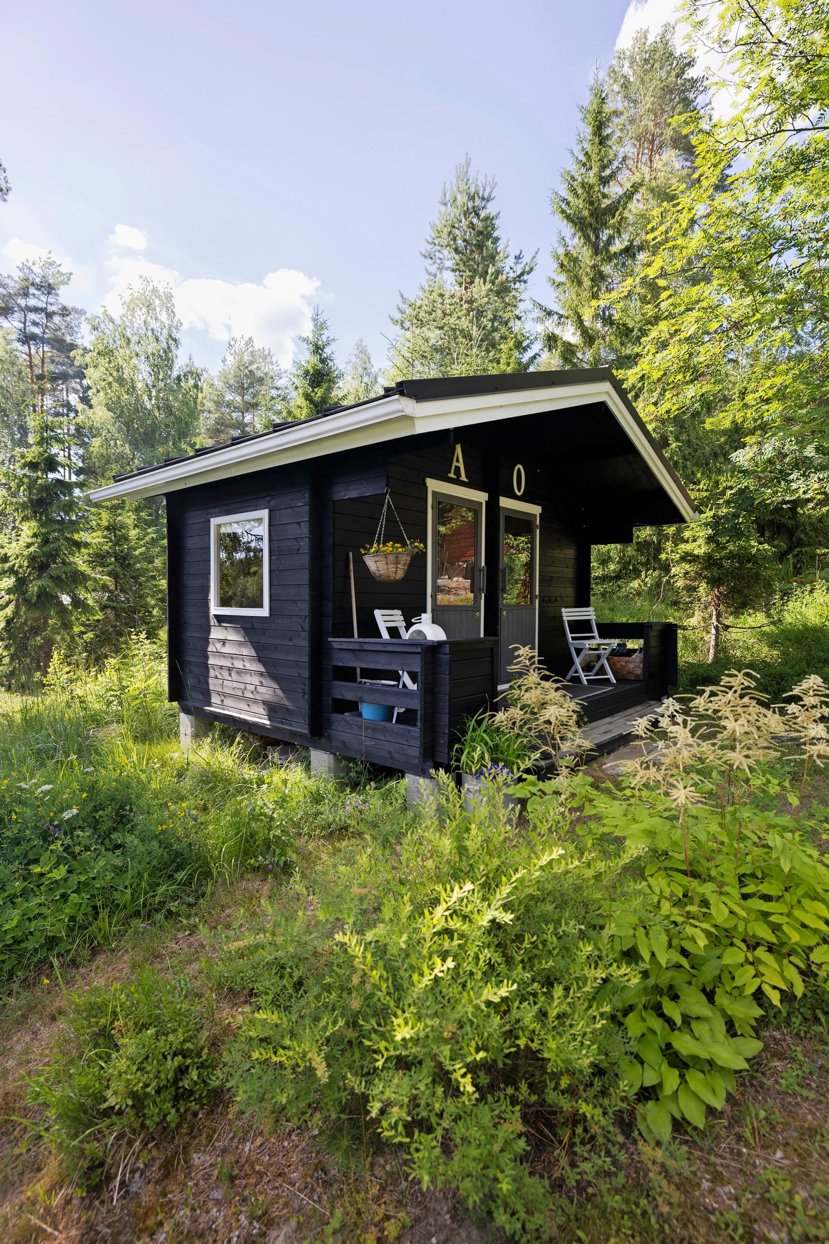 a small black cabin, surrounded by forest and lush garden greenery