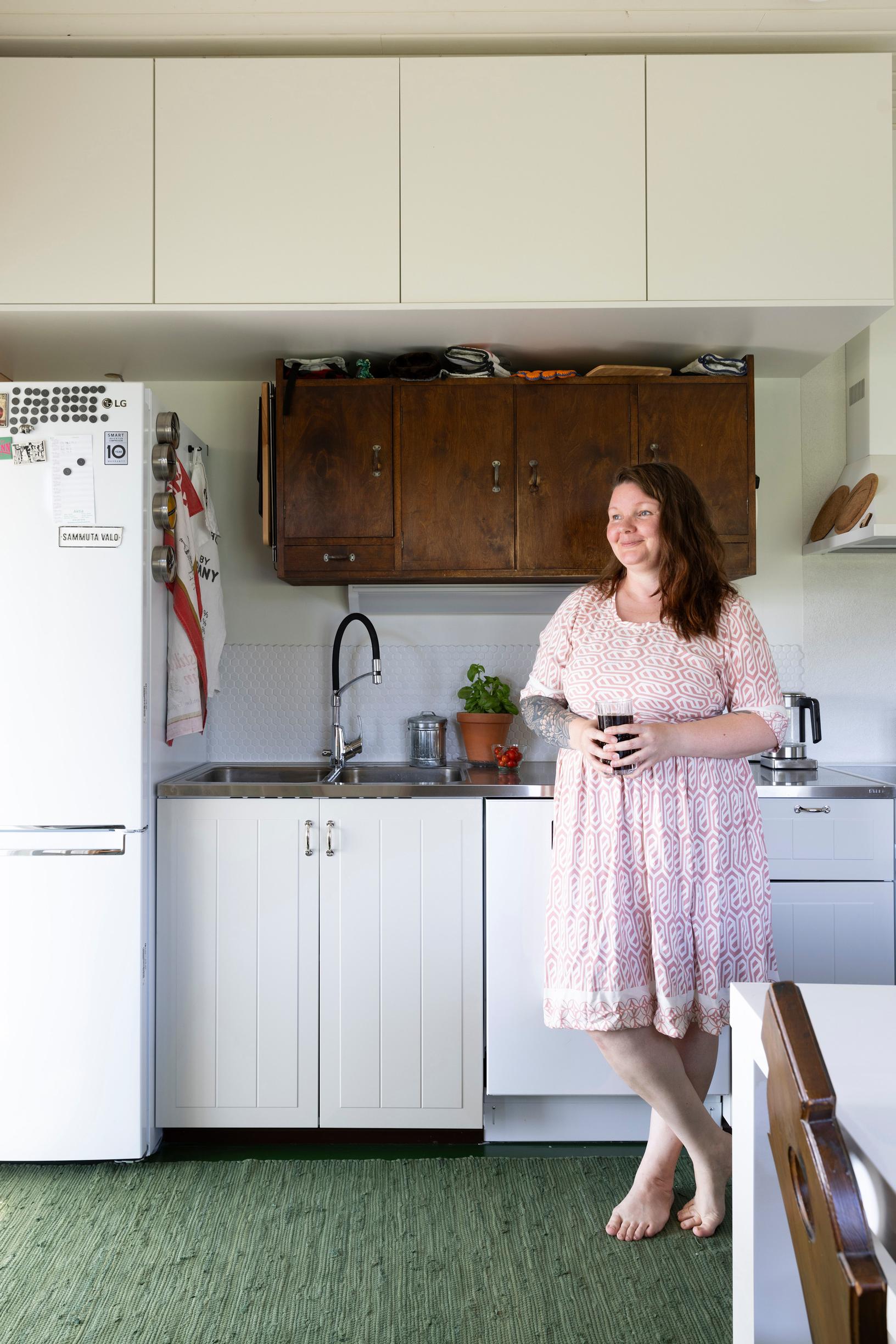 Tiia stands in the kitchen wearing a pink dress.