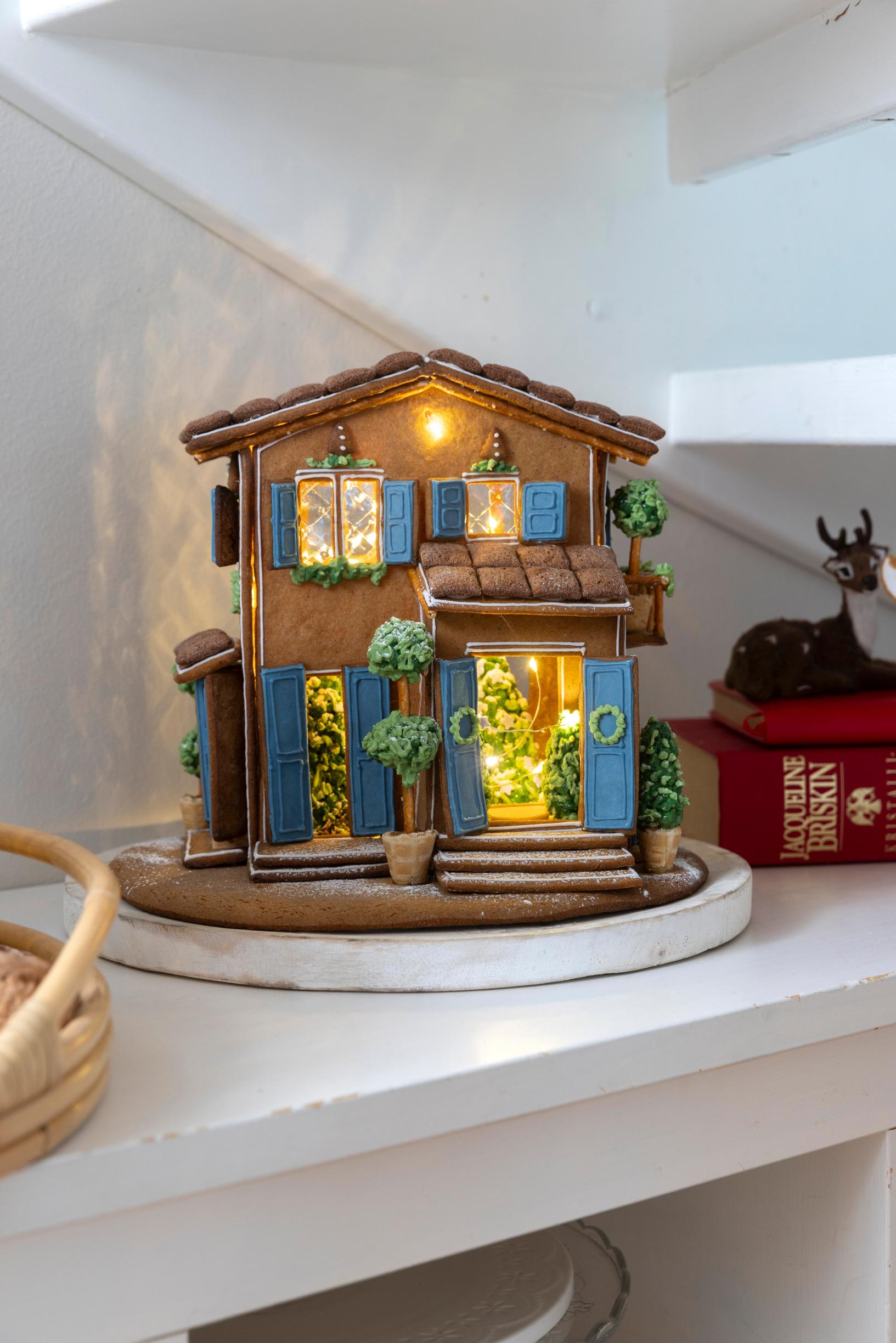 A Mamma Mia–style gingerbread house with blue doors and window frames, adorned with plenty of “greenery.”