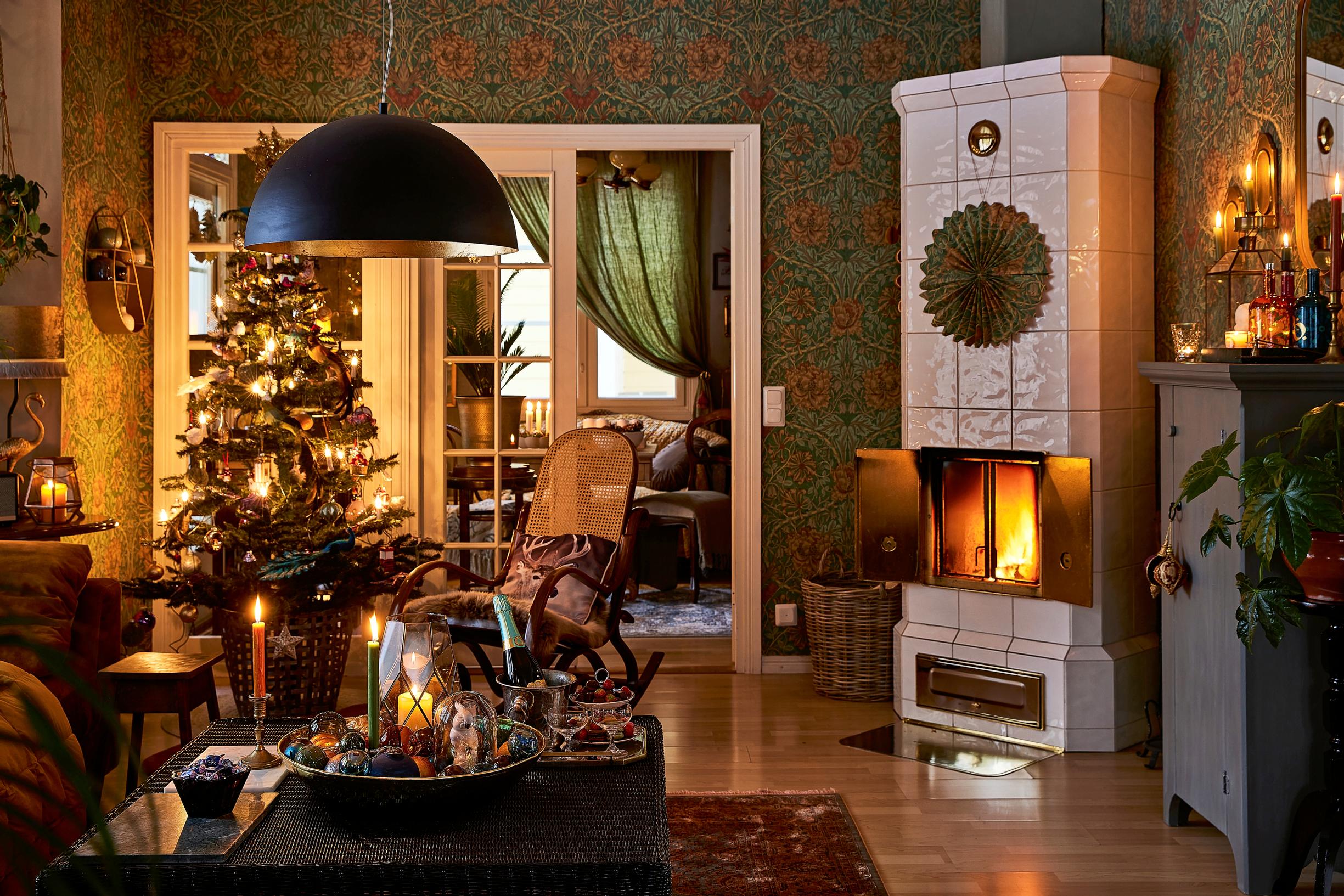 A cozy, Christmasy living room with a tiled stove, Christmas tree, and treats on the table.