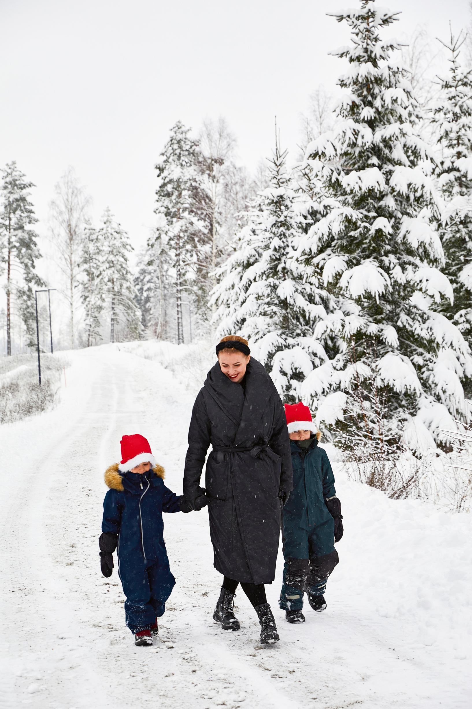 Julia and little boys wearing elf hats walking on a snowy forest path