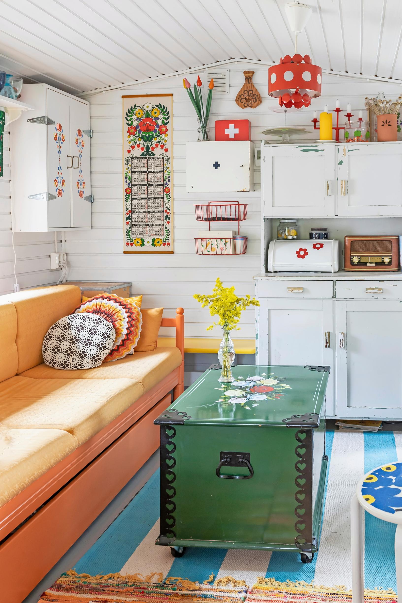 a green vintage trunk, an orange sofa, and a white cabinet in the background with old items