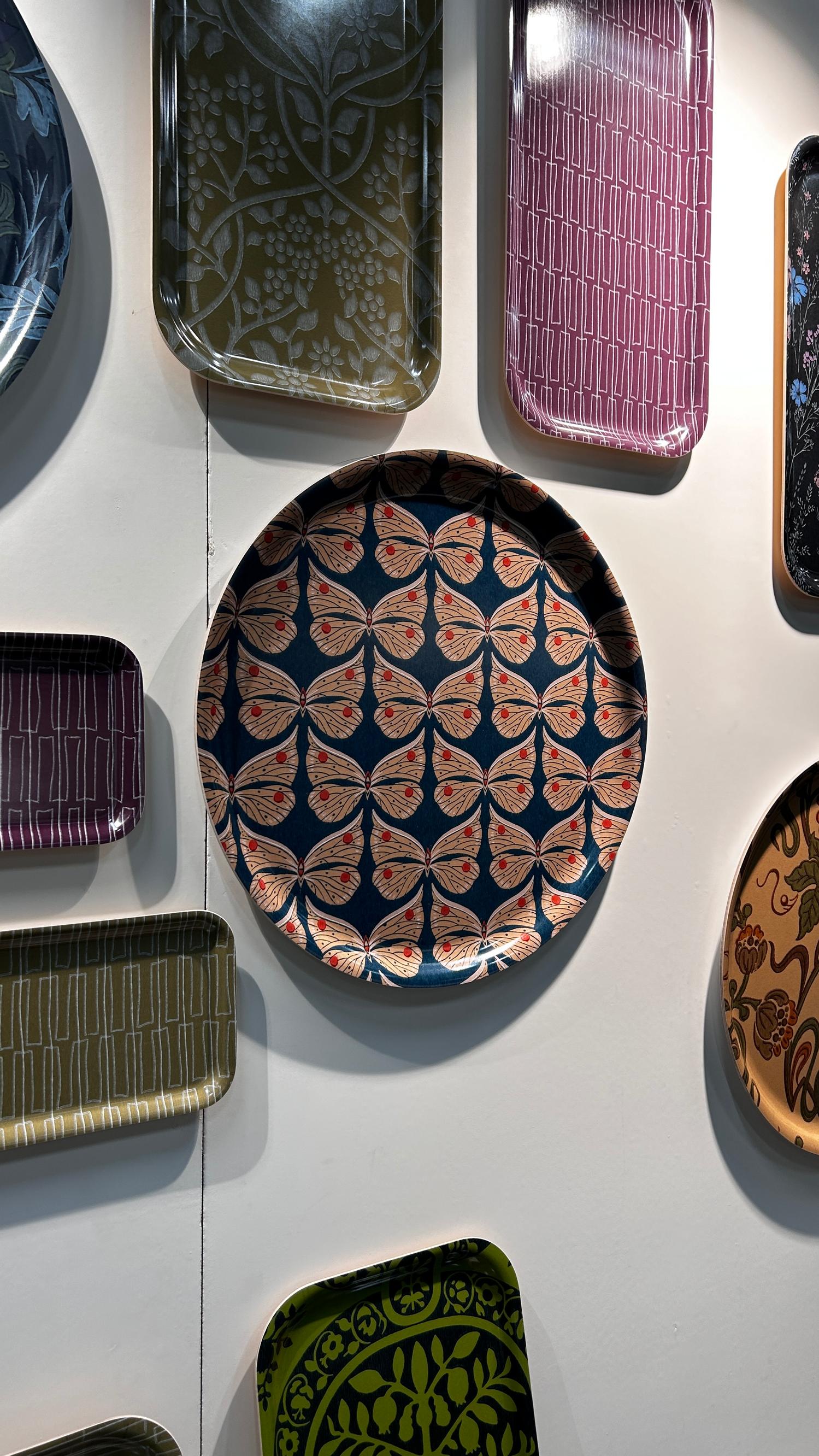 A Pihlgren ja Ritola tray with the Perhonen pattern, alongside other trays mounted on the wall.