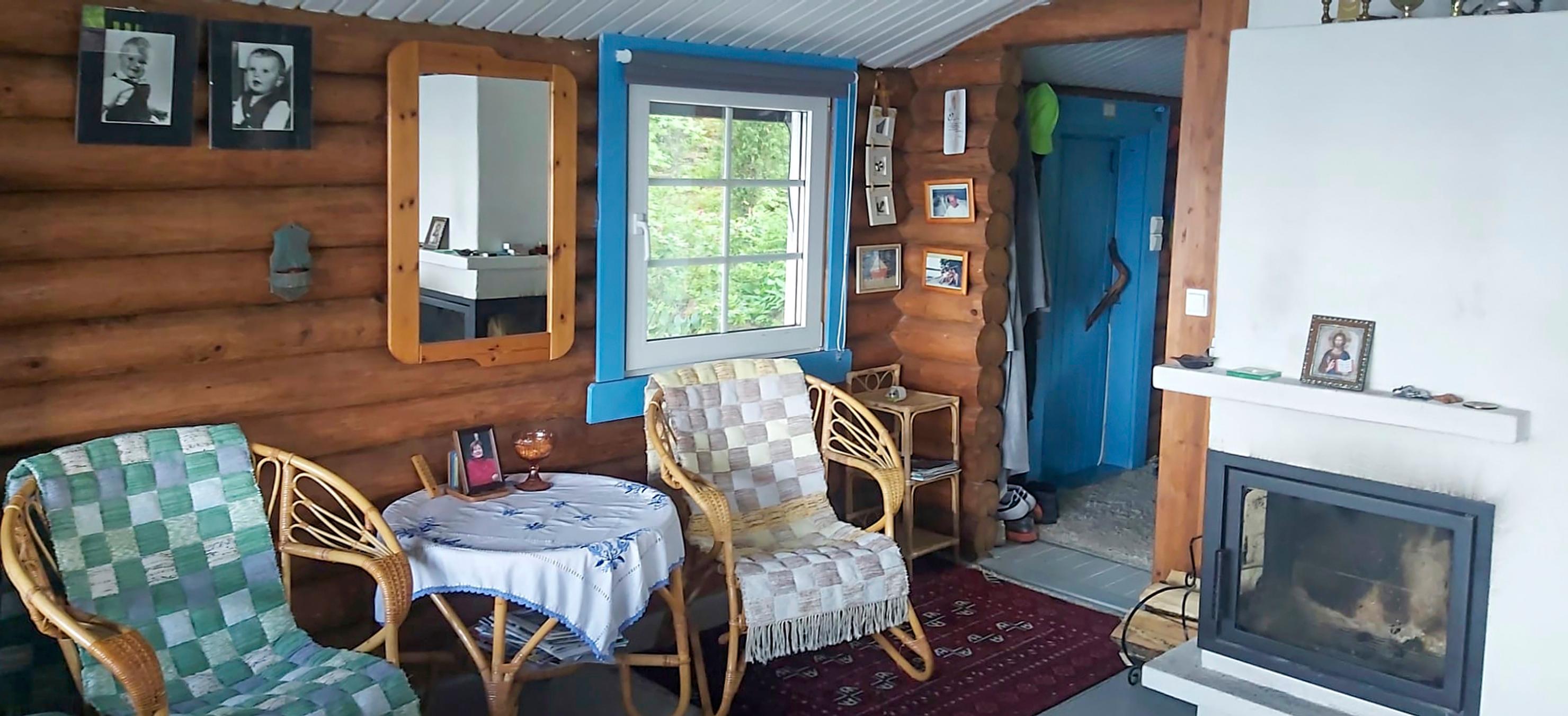 In Singer Petri Laaksonen’s summer cottage, there are rattan chairs and a table, round-log walls, a mirror, and a white fireplace