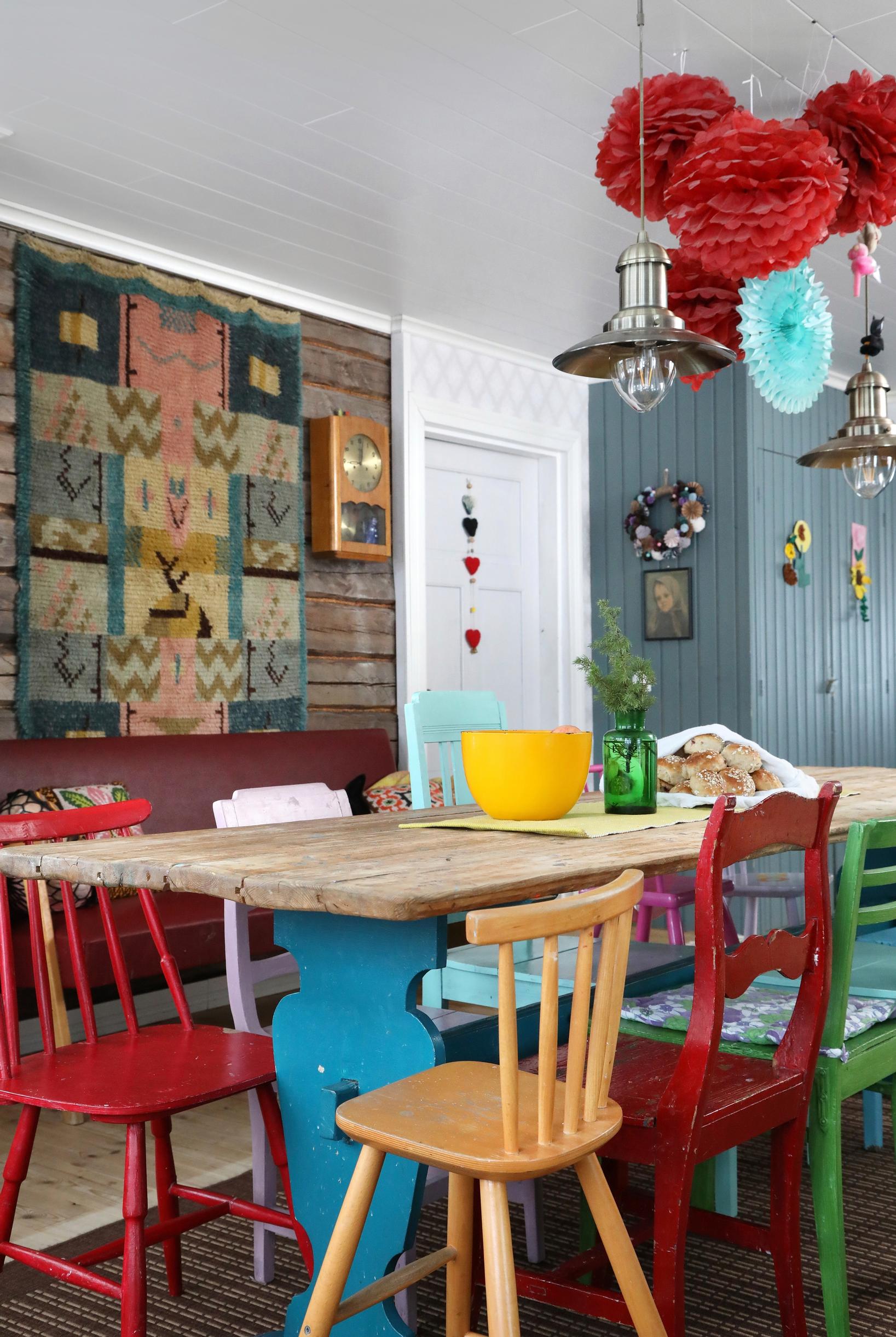 A dining table made from old planks and chairs in different colors.