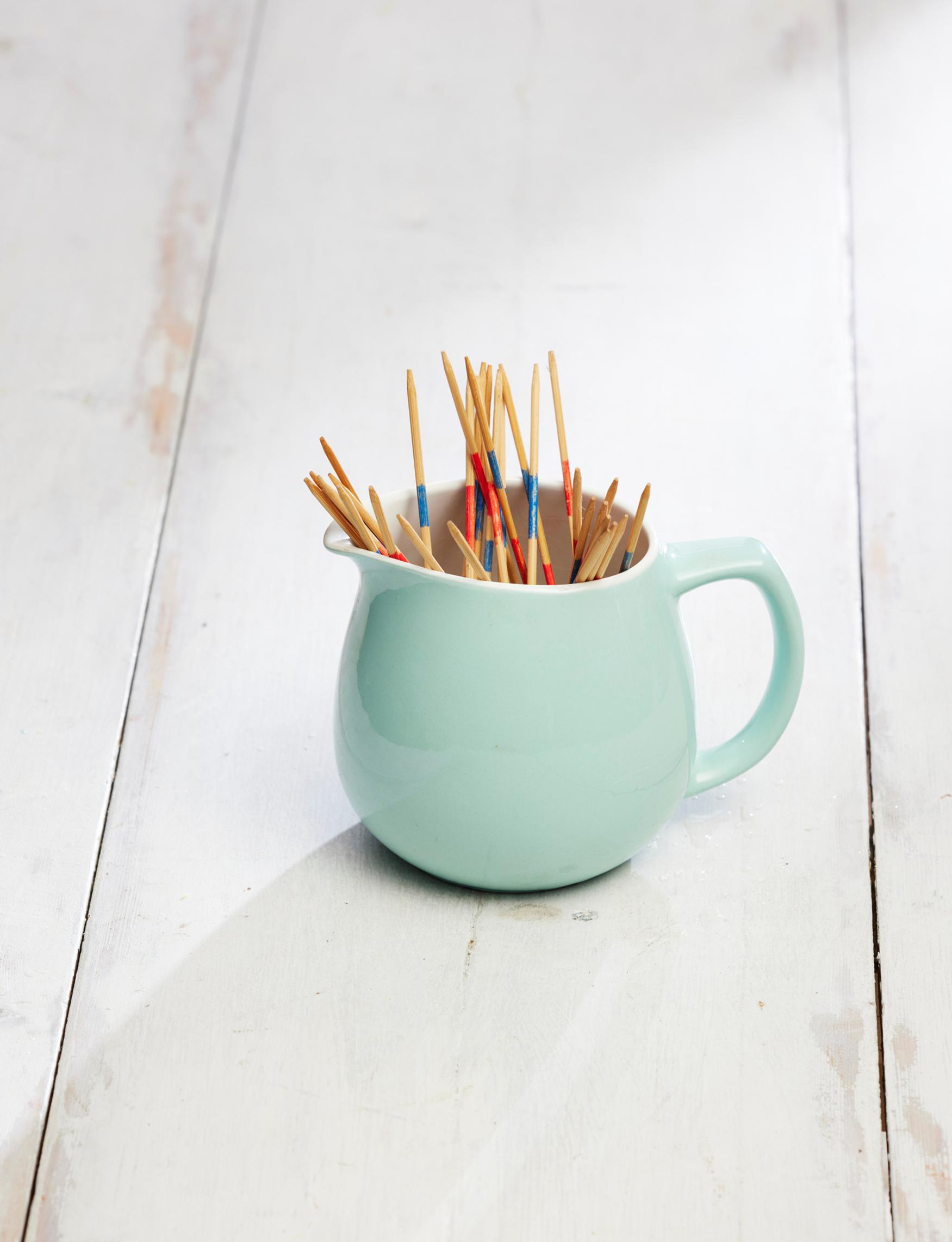 An old Arabia milk pitcher holding Mikado game sticks.