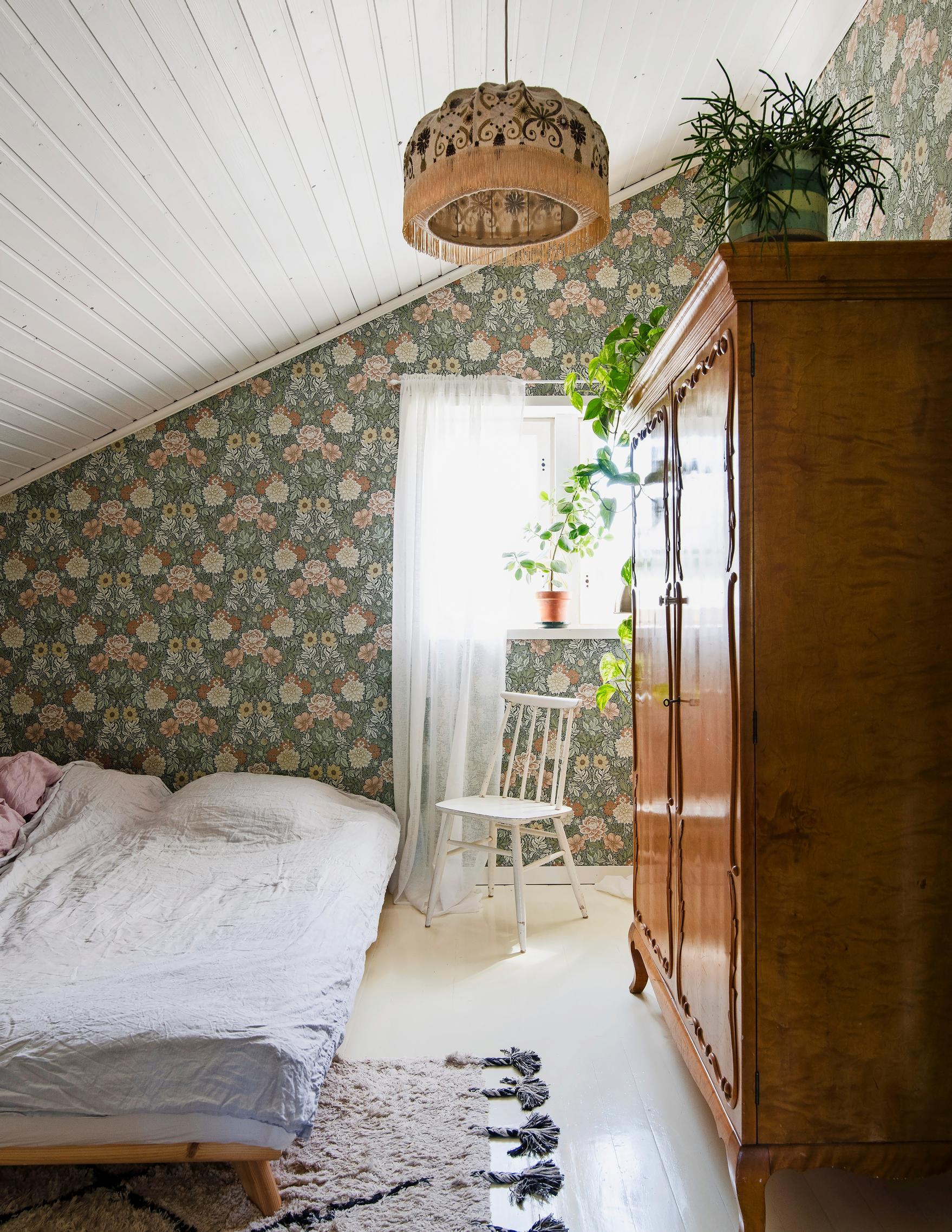 Photo of the bedroom with a slanted ceiling and floral wallpapered wall.