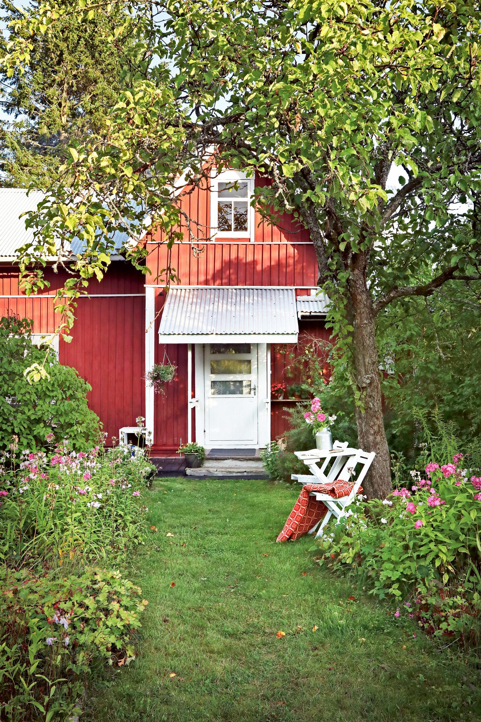 An old red wooden house with garden furniture and flower beds in front