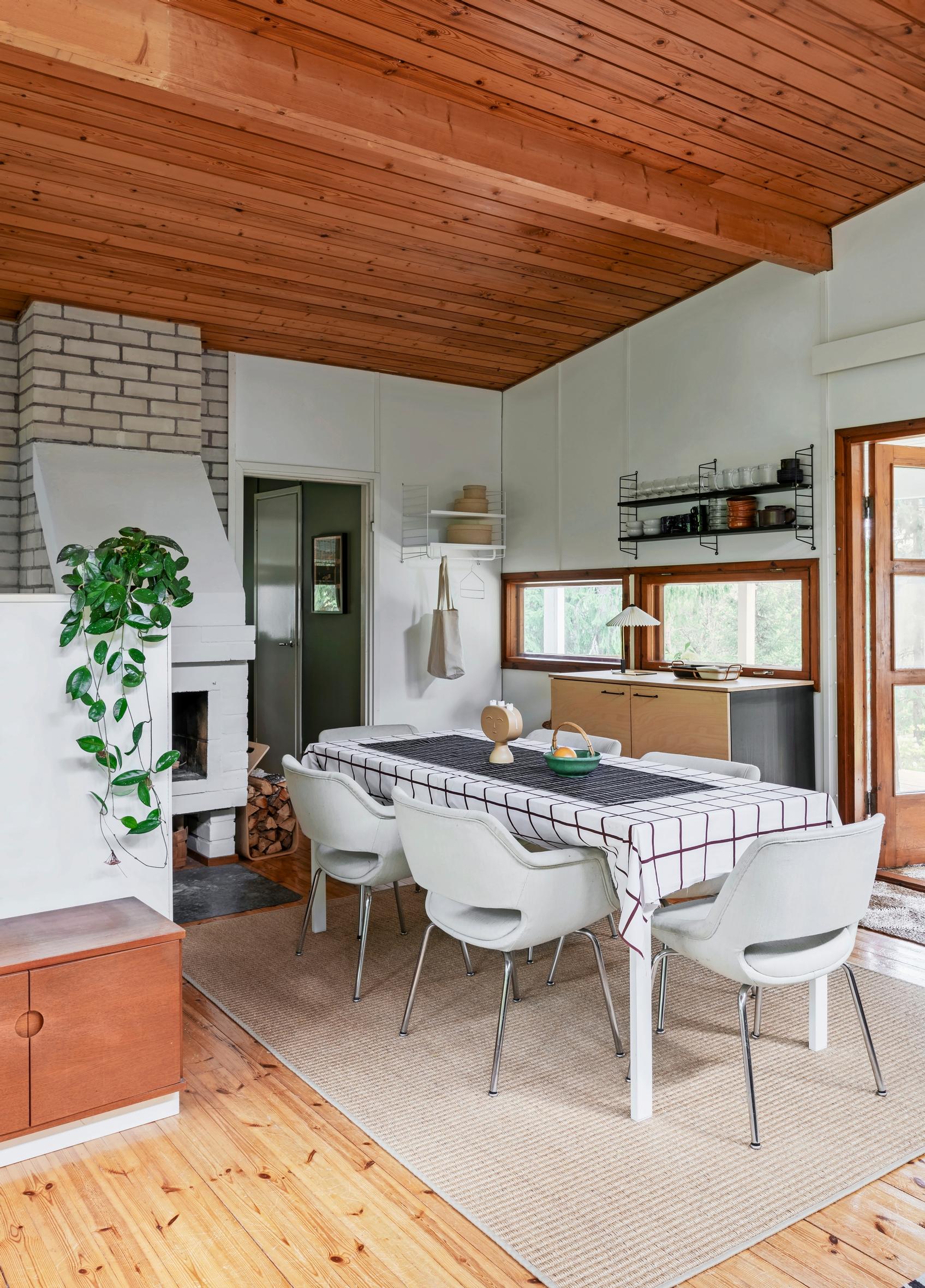 Kitchen in Immonen ja Tammela's cottage, white chairs, checkered tablecloth, and fireplace.