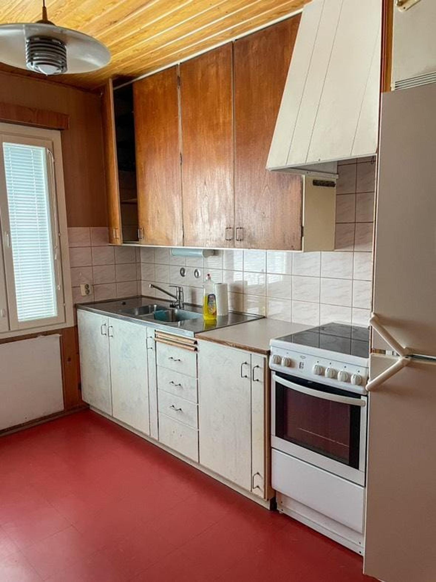 The kitchen features a red floor, painted wooden lower cabinets, and wood-veneer upper cabinets