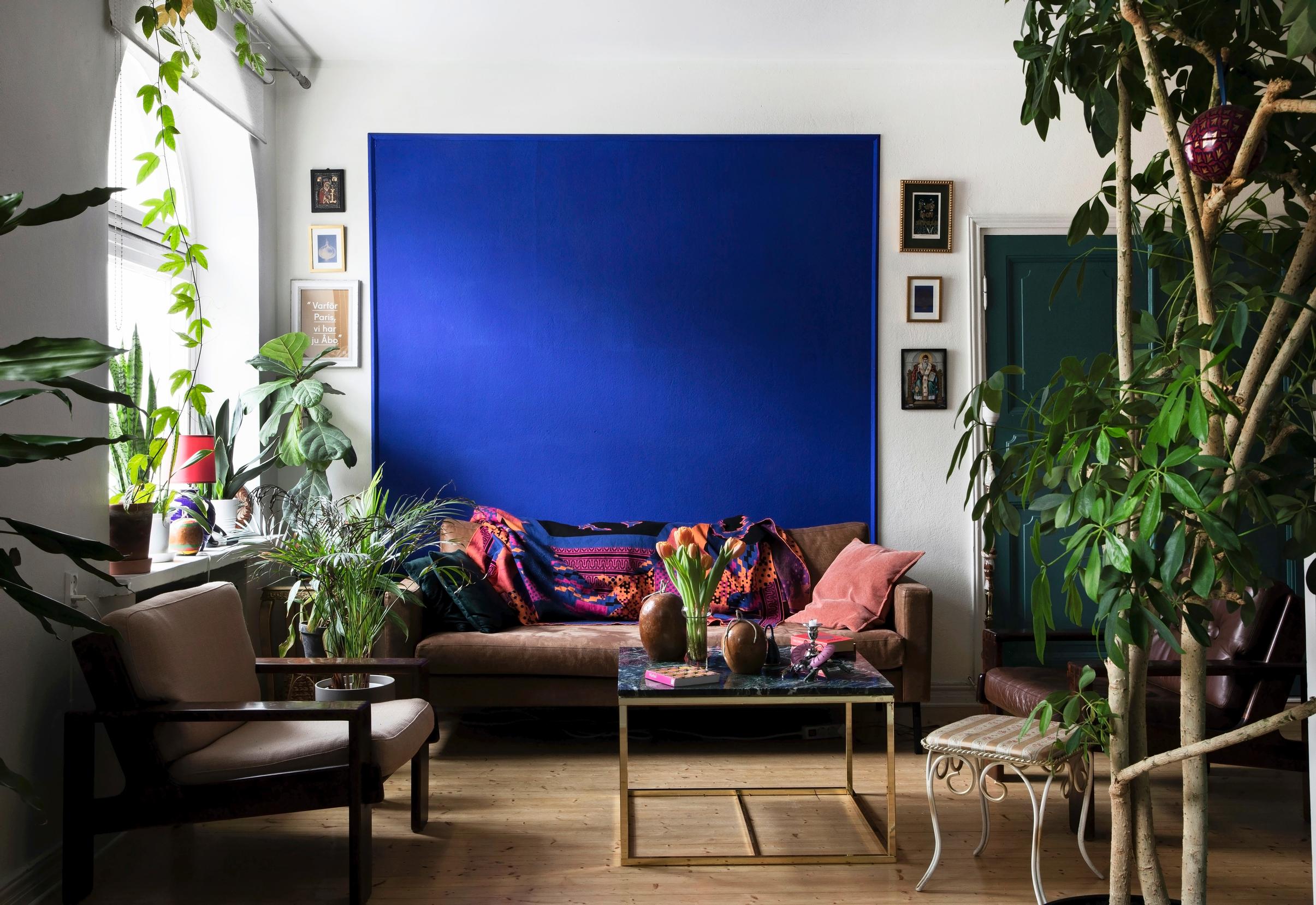 On a white wall, there’s a large blue rectangular area, in front of which is a brown sofa.