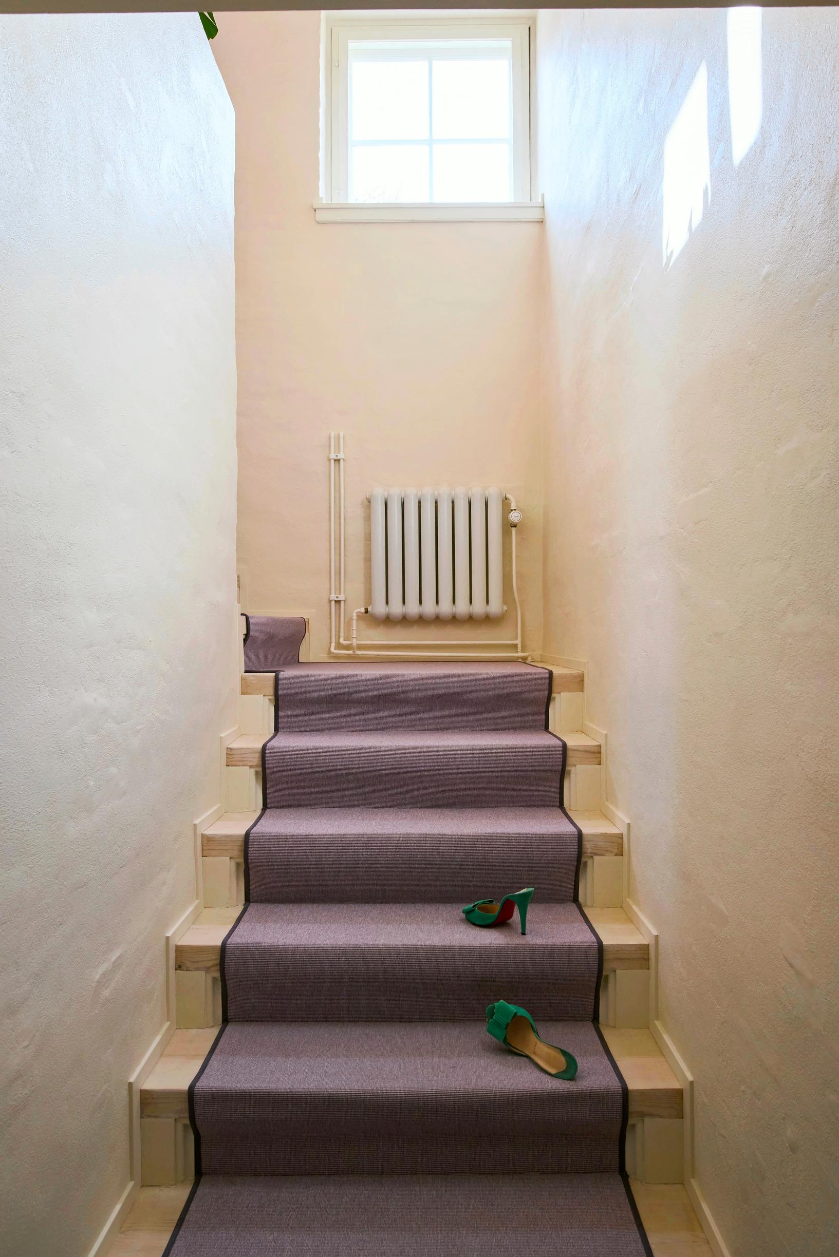 A staircase leading upstairs, covered with a lilac-toned carpet